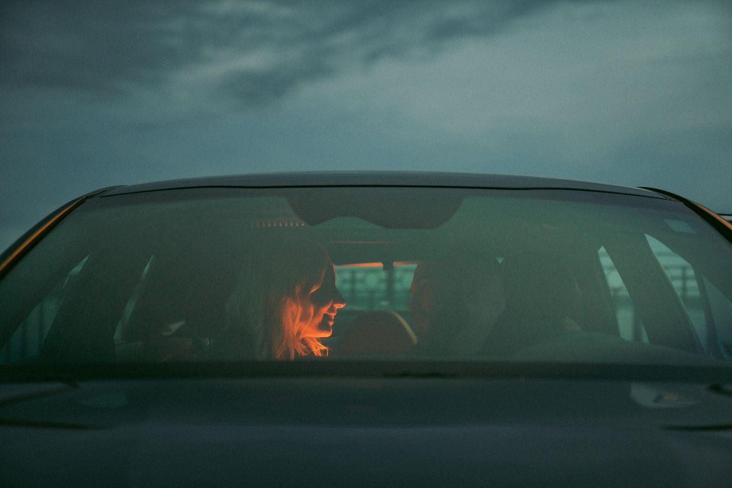 Moody overcast sky reflects on the windshield of a parked car. Couple in Bar Harbor Maine