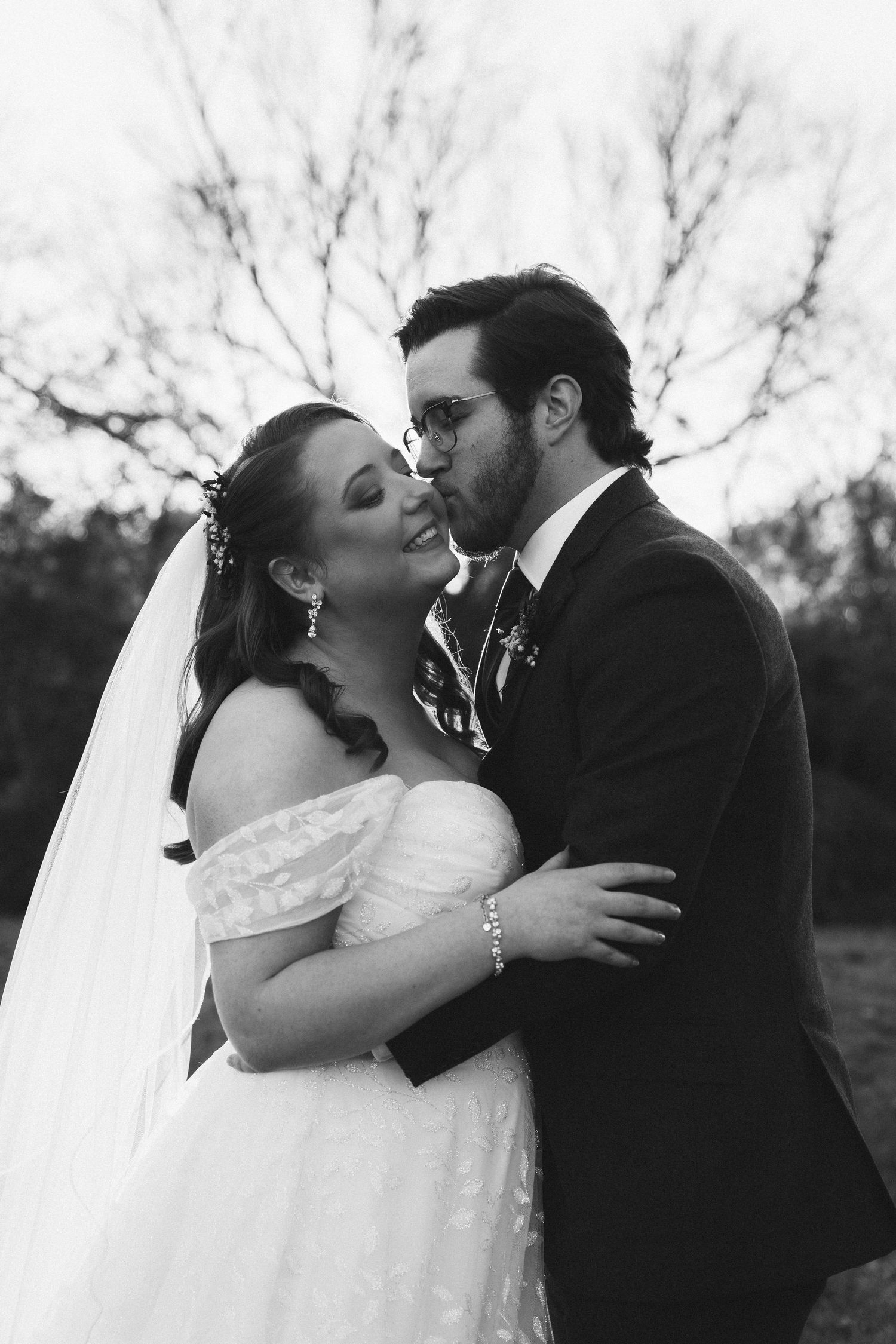 Black and white intimate wedding portrait against bare winter trees.