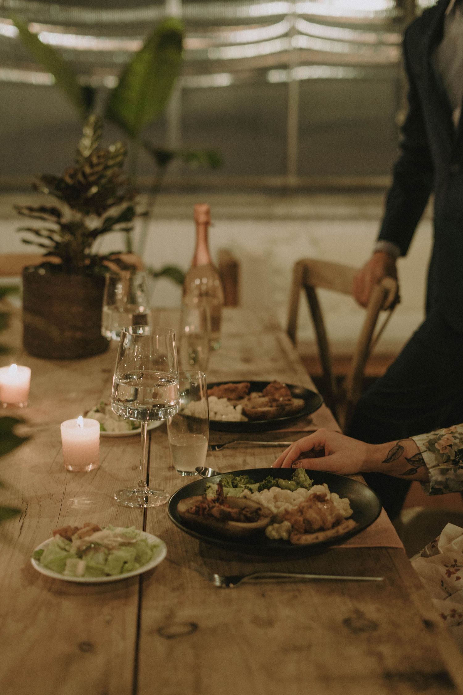 An intimate dinner table setting with candles, wine glasses and plated food.