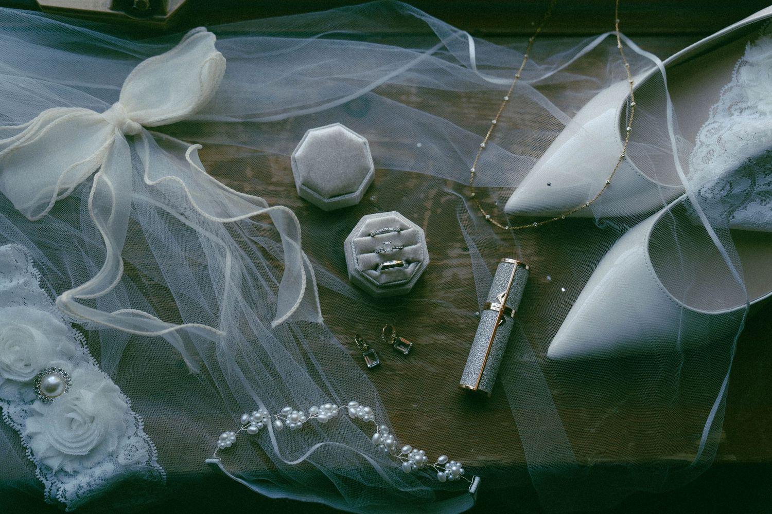 Wedding accessories including veil, ribbon, and jewelry arranged on dark surface.