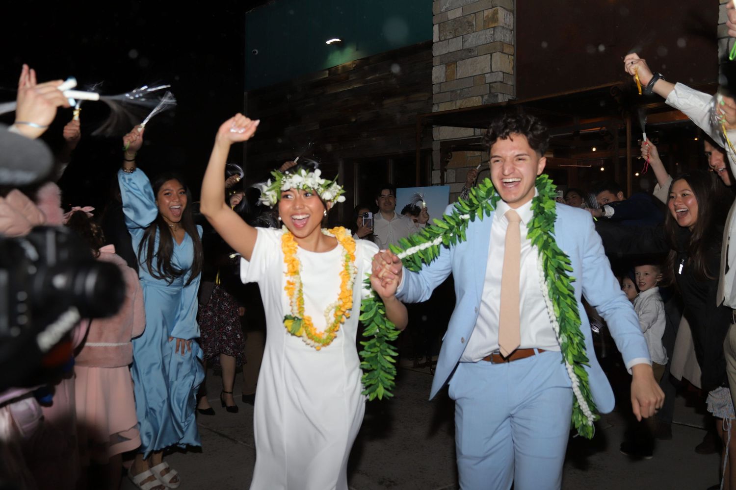 Wedding guests dance and celebrate during an energetic reception party with yellow leis and blue attire.