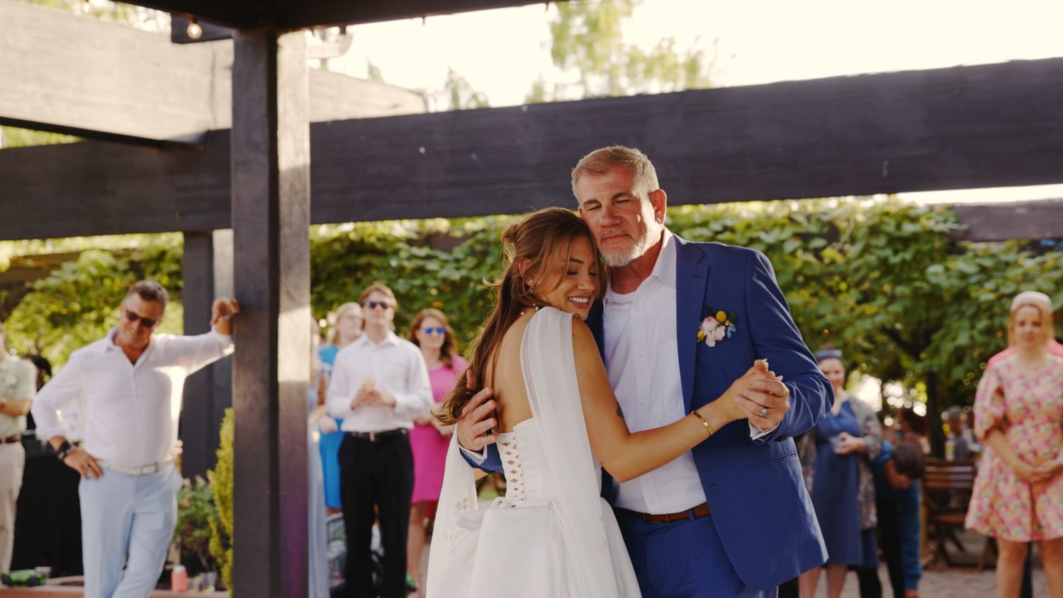 A couple dances together at their outdoor wedding reception while guests look on in the background.