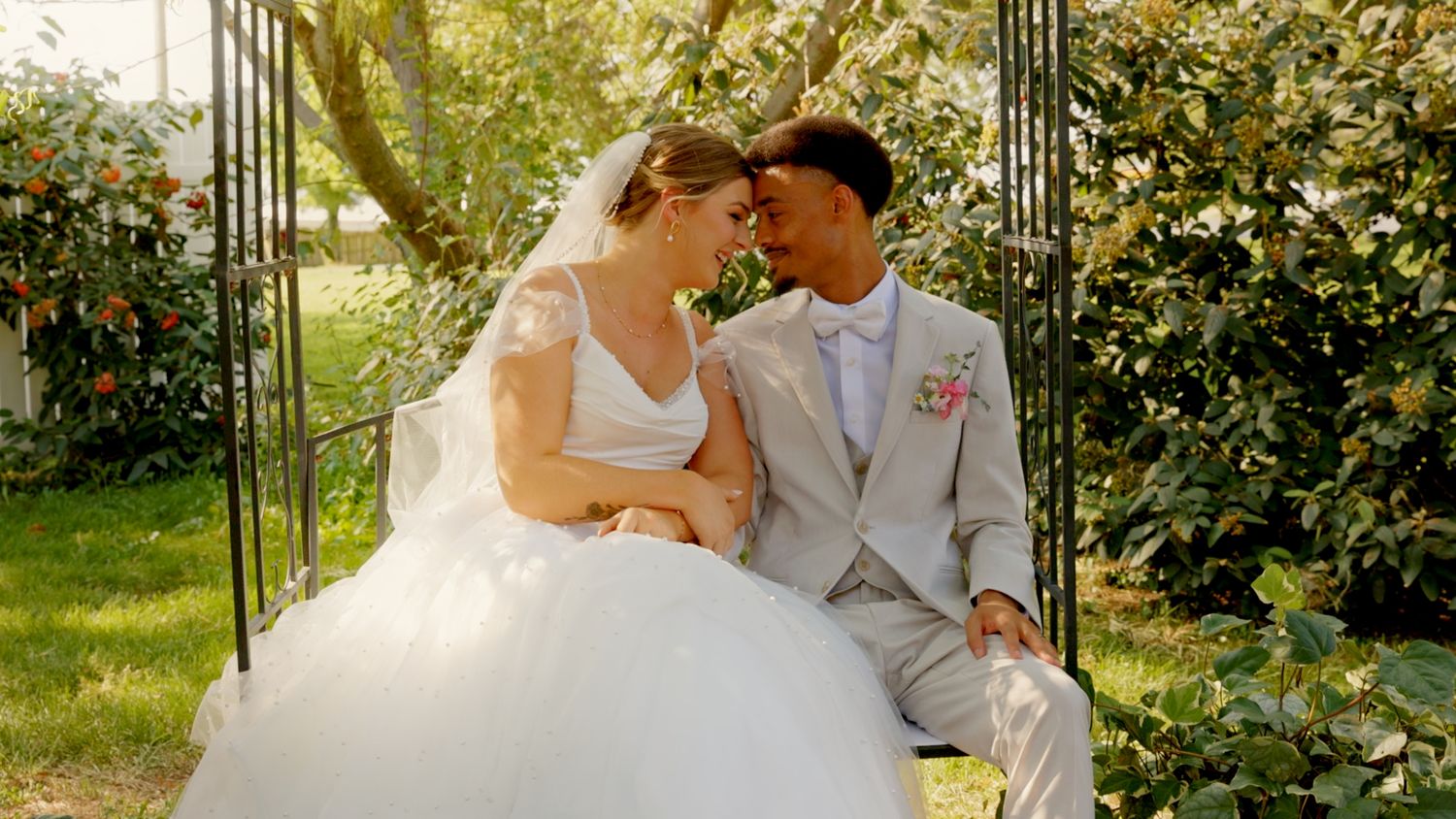 Bride and groom sitting together in a garden gazebo, sharing a romantic glance on their wedding day.