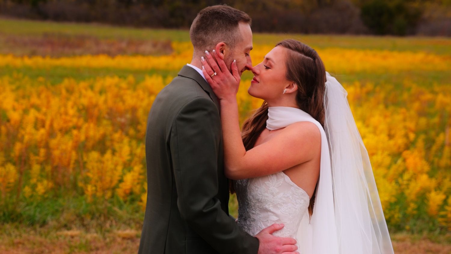 Bride and groom sharing a romantic kiss in front of vibrant yellow autumn fields on their wedding day.