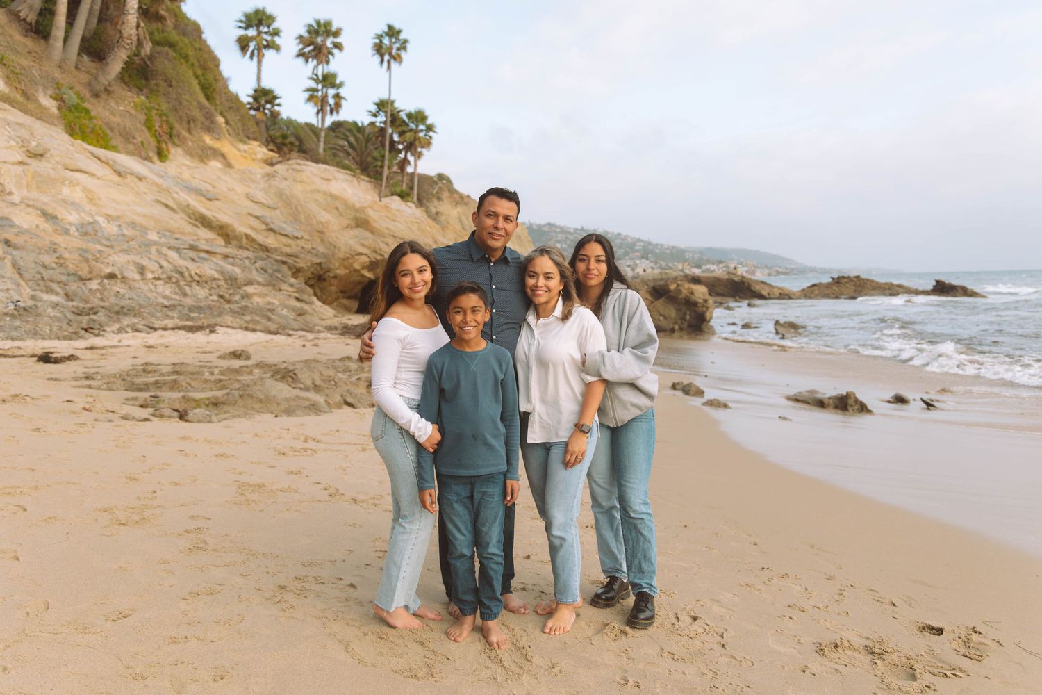 Group photo on a scenic beach with palm trees and rocky coastline during daytime.