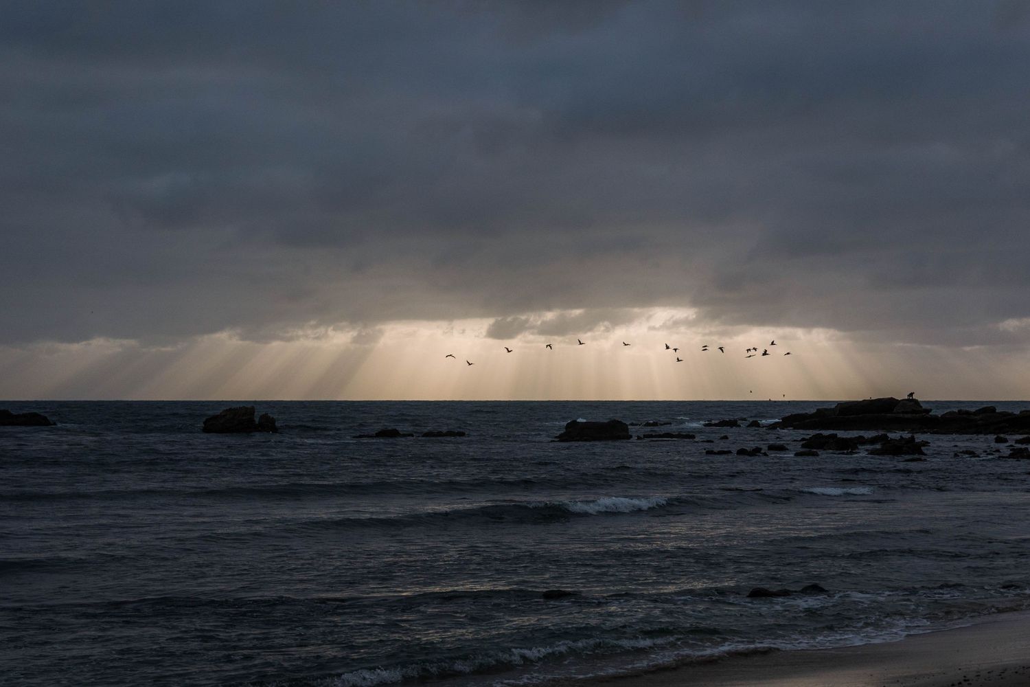 Dramatic stormy seascape with sun rays piercing through dark clouds over rough ocean waters.