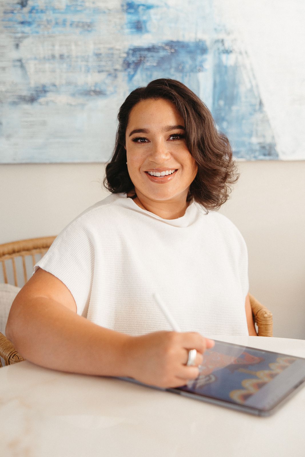 Person in white t-shirt smiling while working on a tablet at a table.