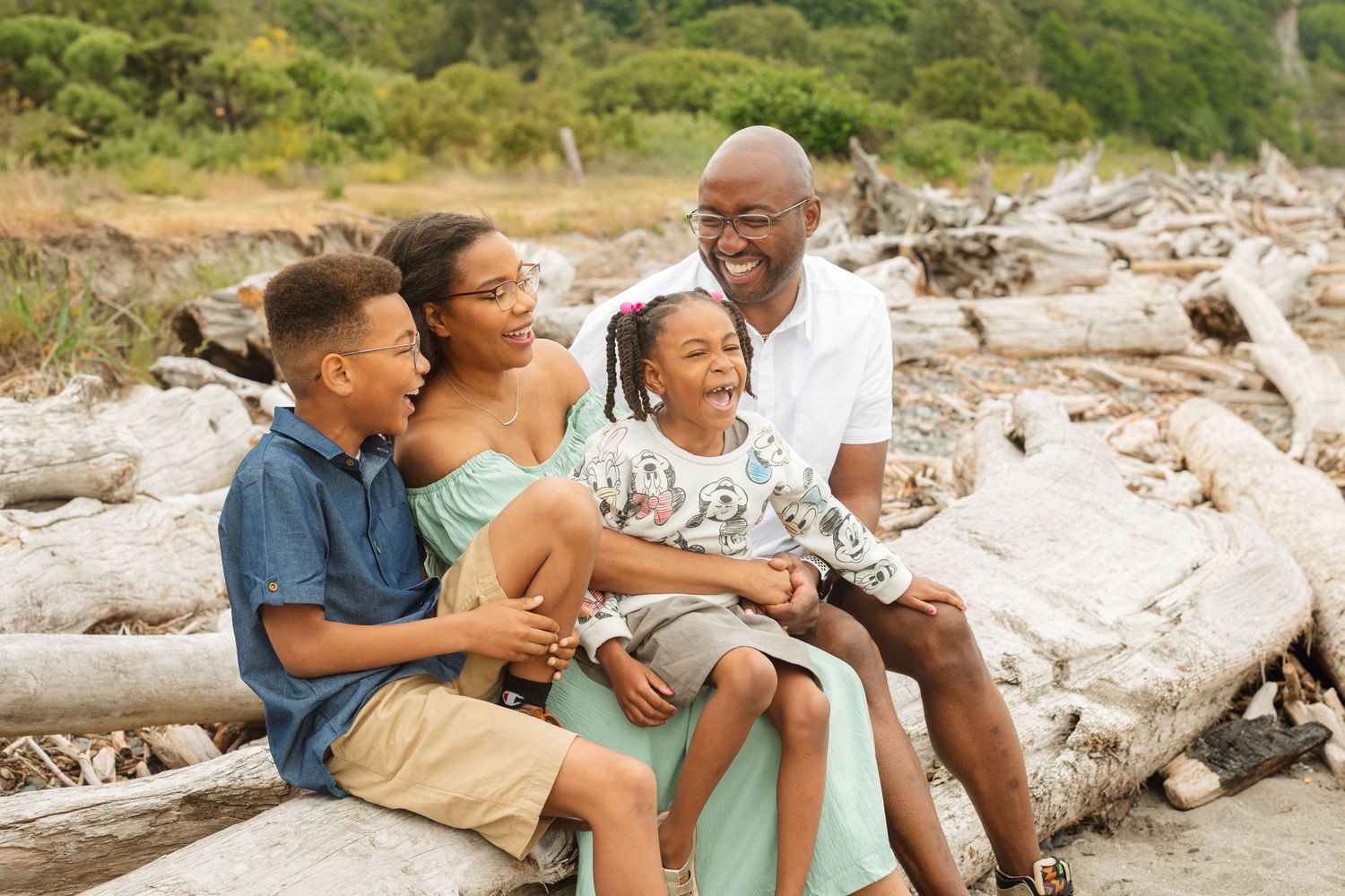 Family sharing joyful moment while sitting together on beach driftwood in Discovery Park, Seattle.