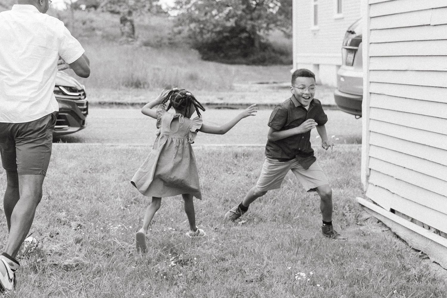 Black and white photo of children playing and running in a backyard near a house.