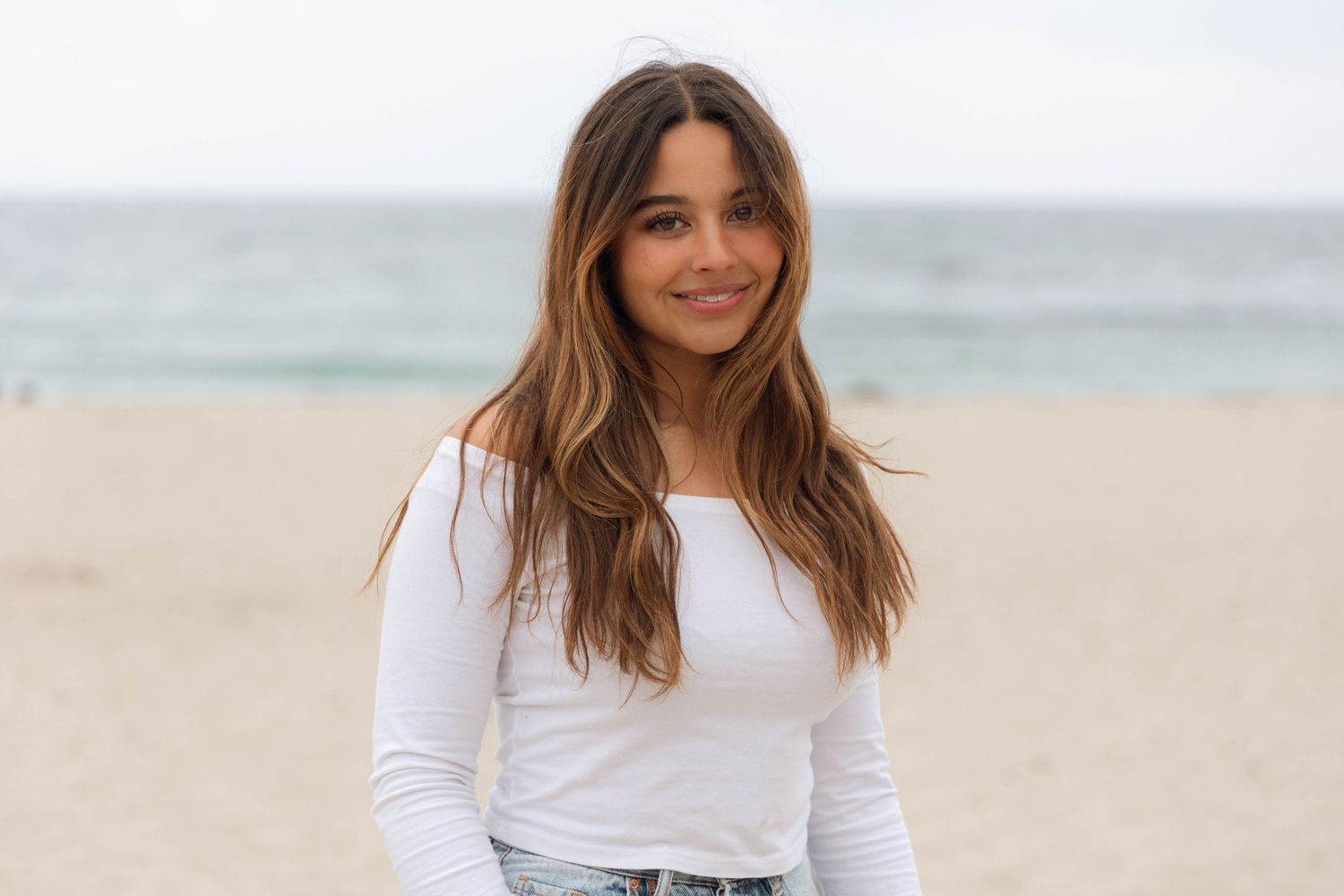 Person in white long sleeve shirt smiling at beach.