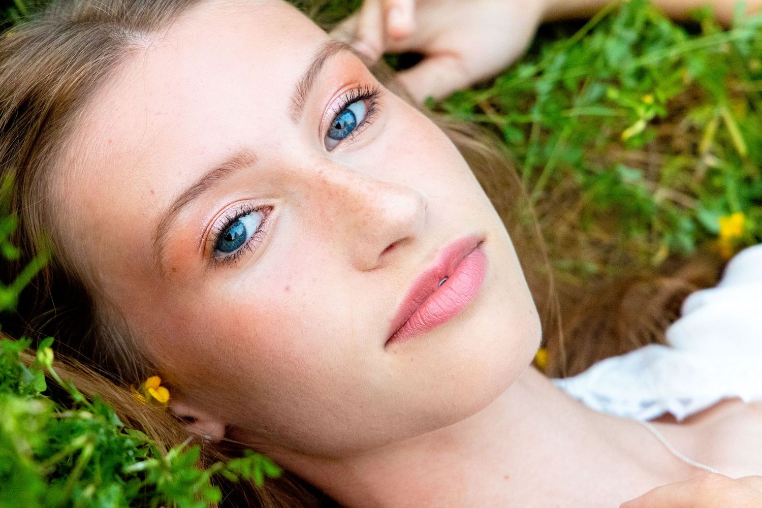 Close up portrait of person with striking blue eyes lying in grass with flowers.