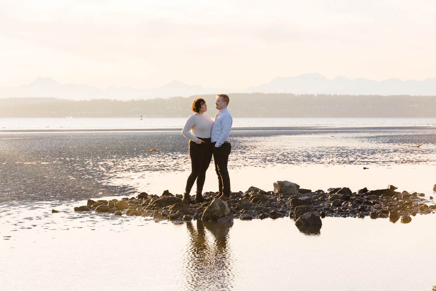 Silhouetted couple reflected in tidal waters during golden hour.