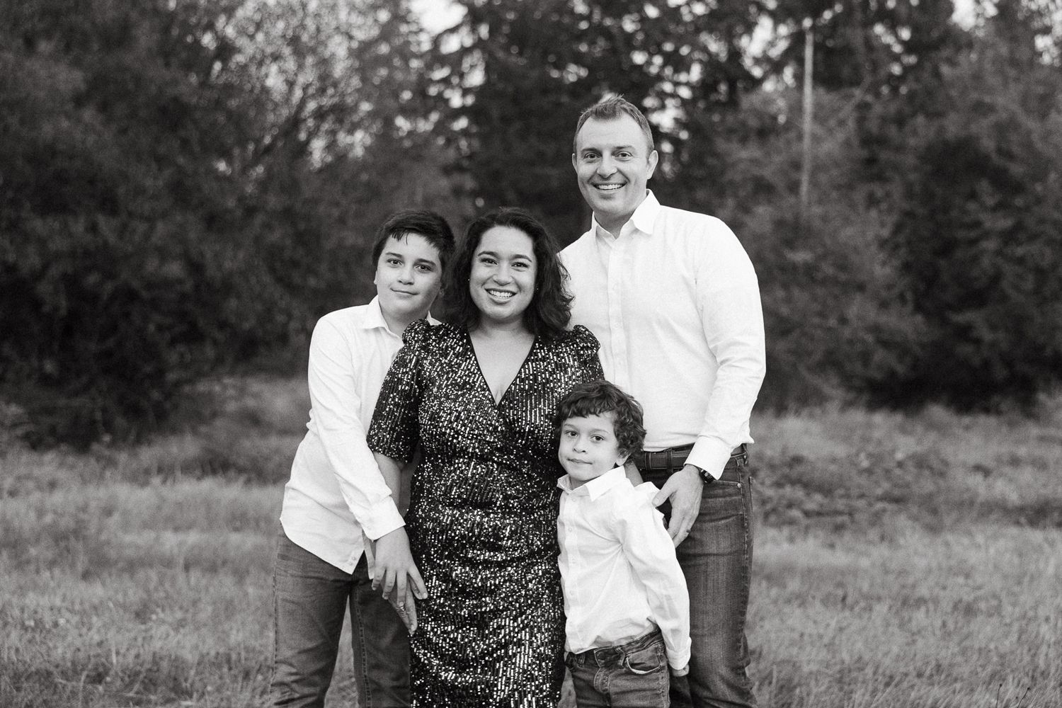 Black and white portrait of a family of four standing together outdoors in a natural setting.