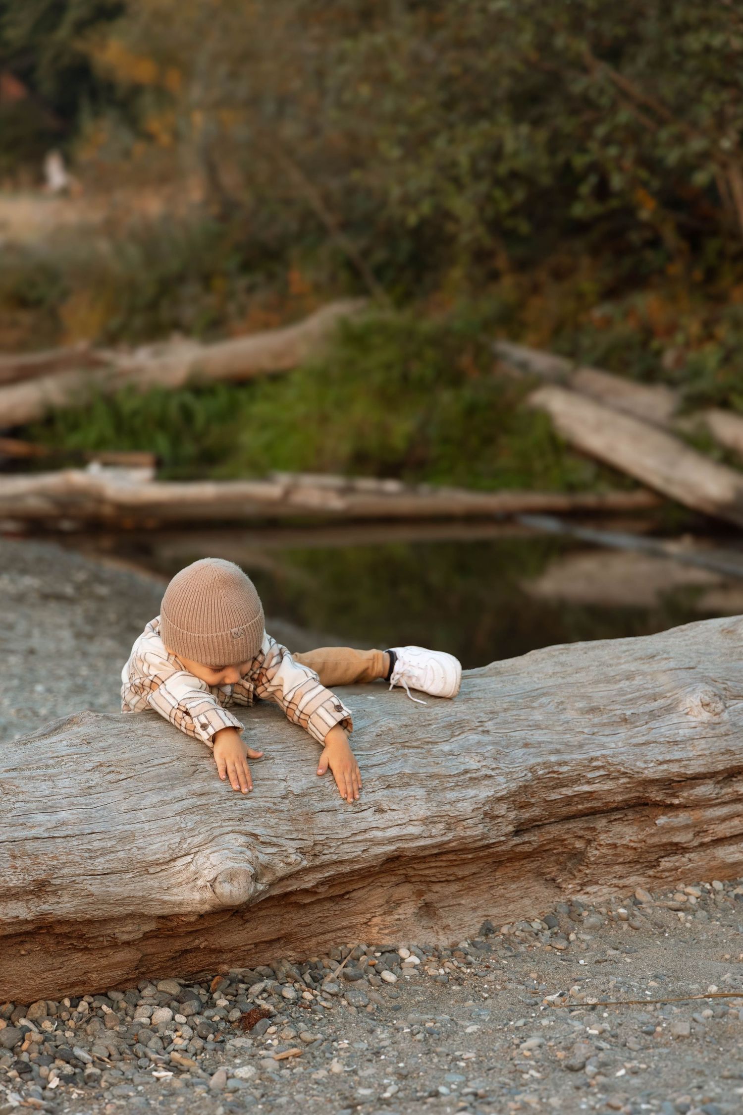 A small child explores and plays on a large driftwood log near a river or stream.