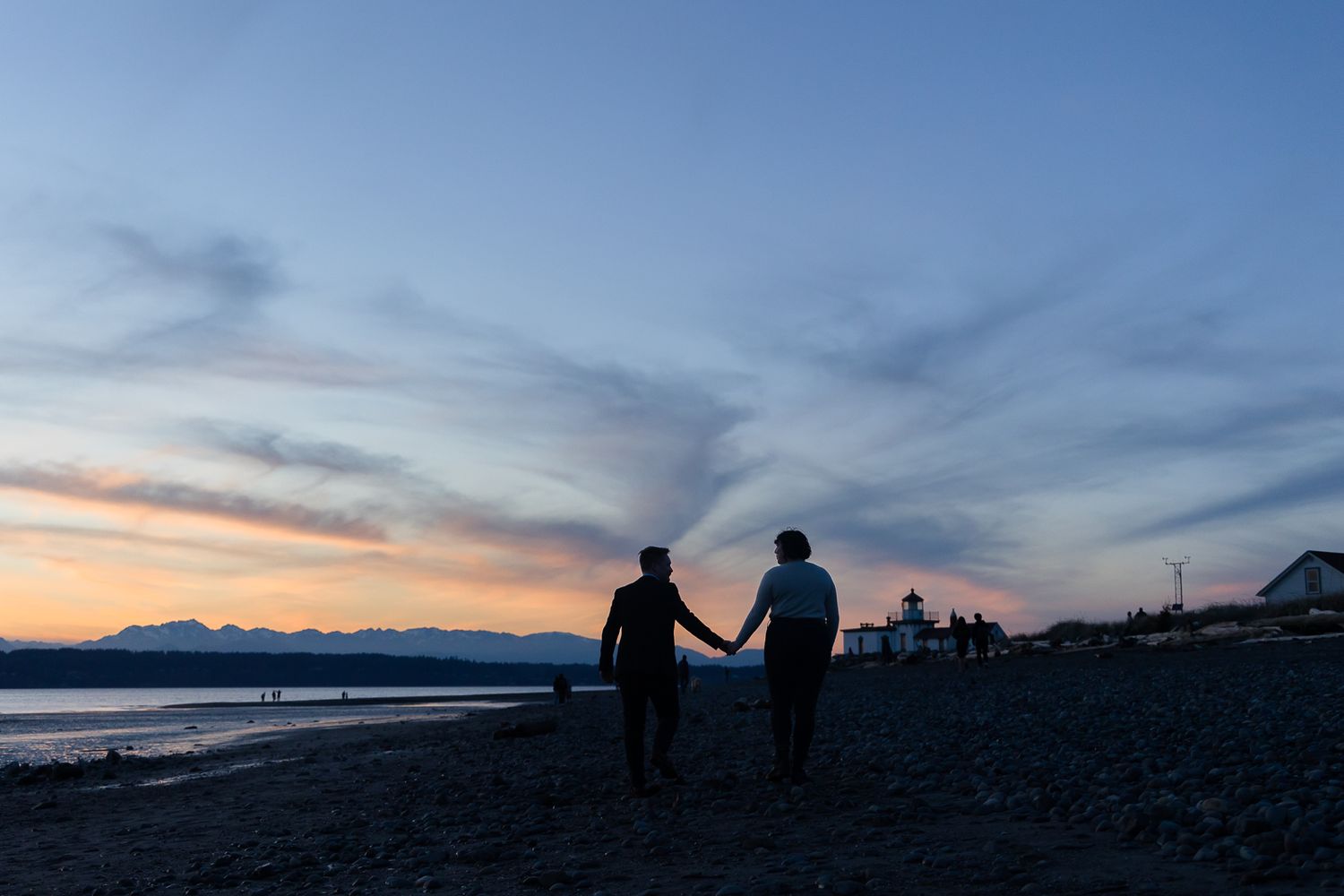 Silhouetted couple holding hands on beach against colorful dusk sky.