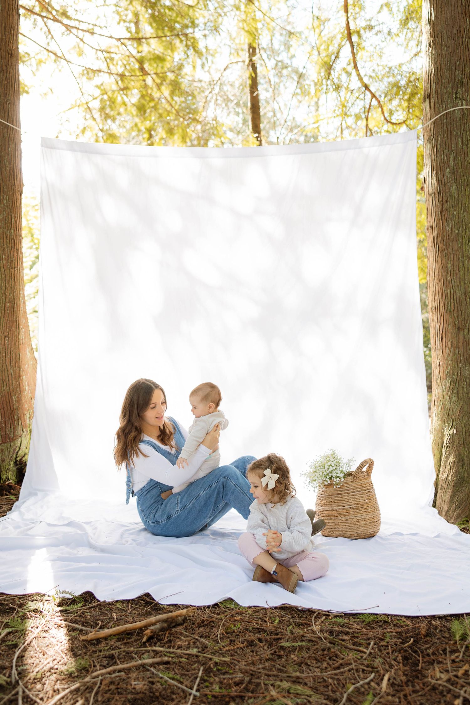 A casual outdoor family portrait session against a white backdrop between trees.