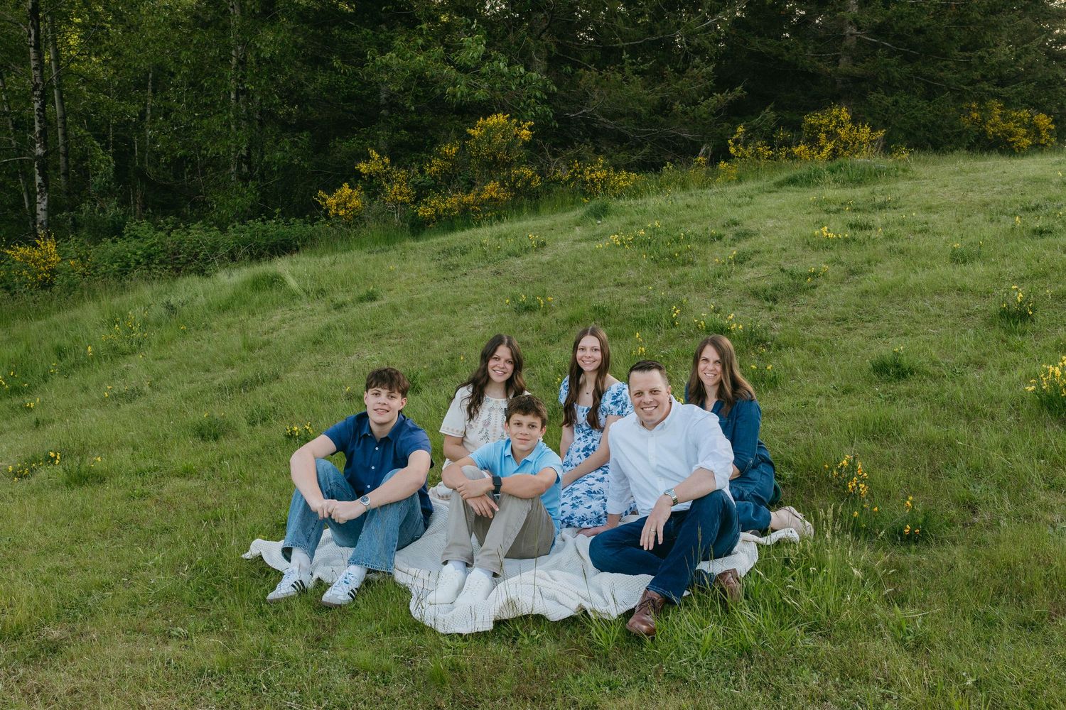 People relax together on a sunny grassy hillside in a casual outdoor setting during summer.