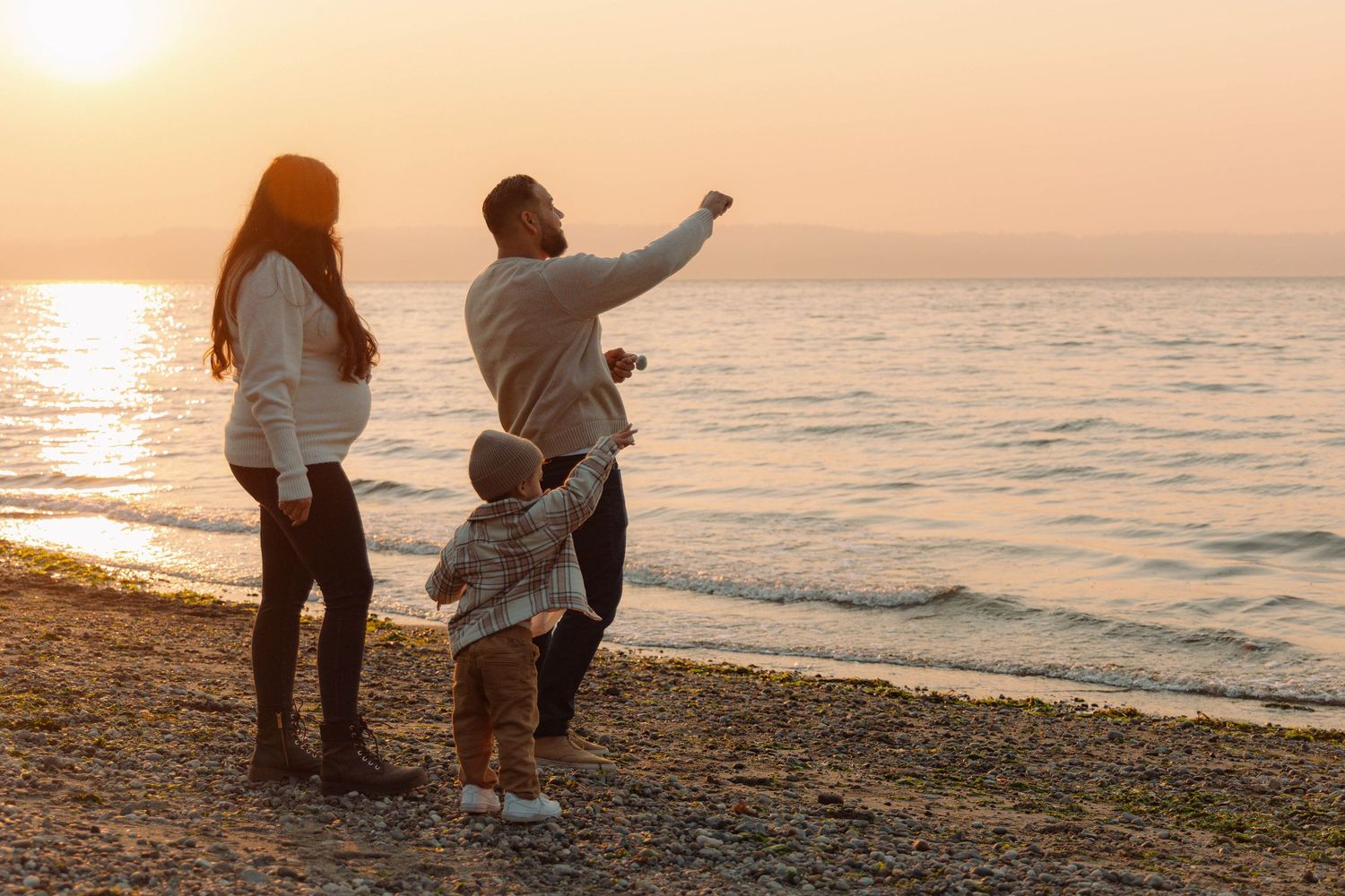 Family watching sunset on beach as parent points towards horizon.