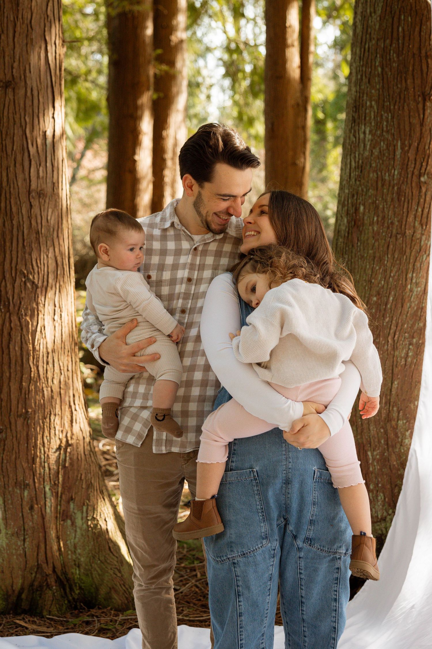 Family sharing tender moment together in sunlit forest setting with two small children.