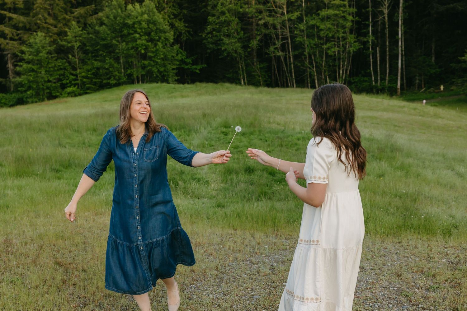 Two people dancing outdoors in a grassy field on a sunny day, one wearing white and one wearing blue denim.