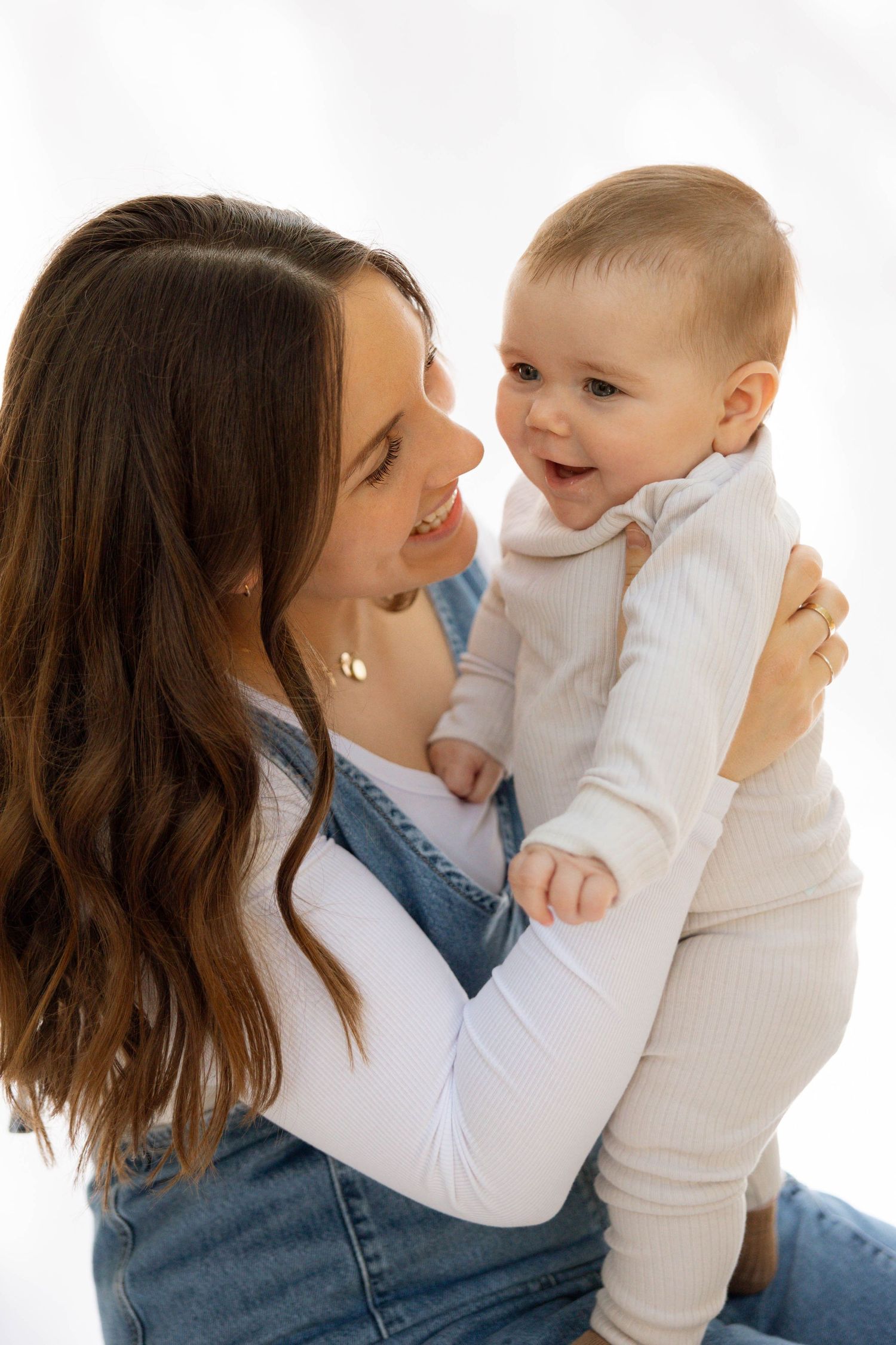 Parent and baby in matching white outfits sharing joyful moment together.