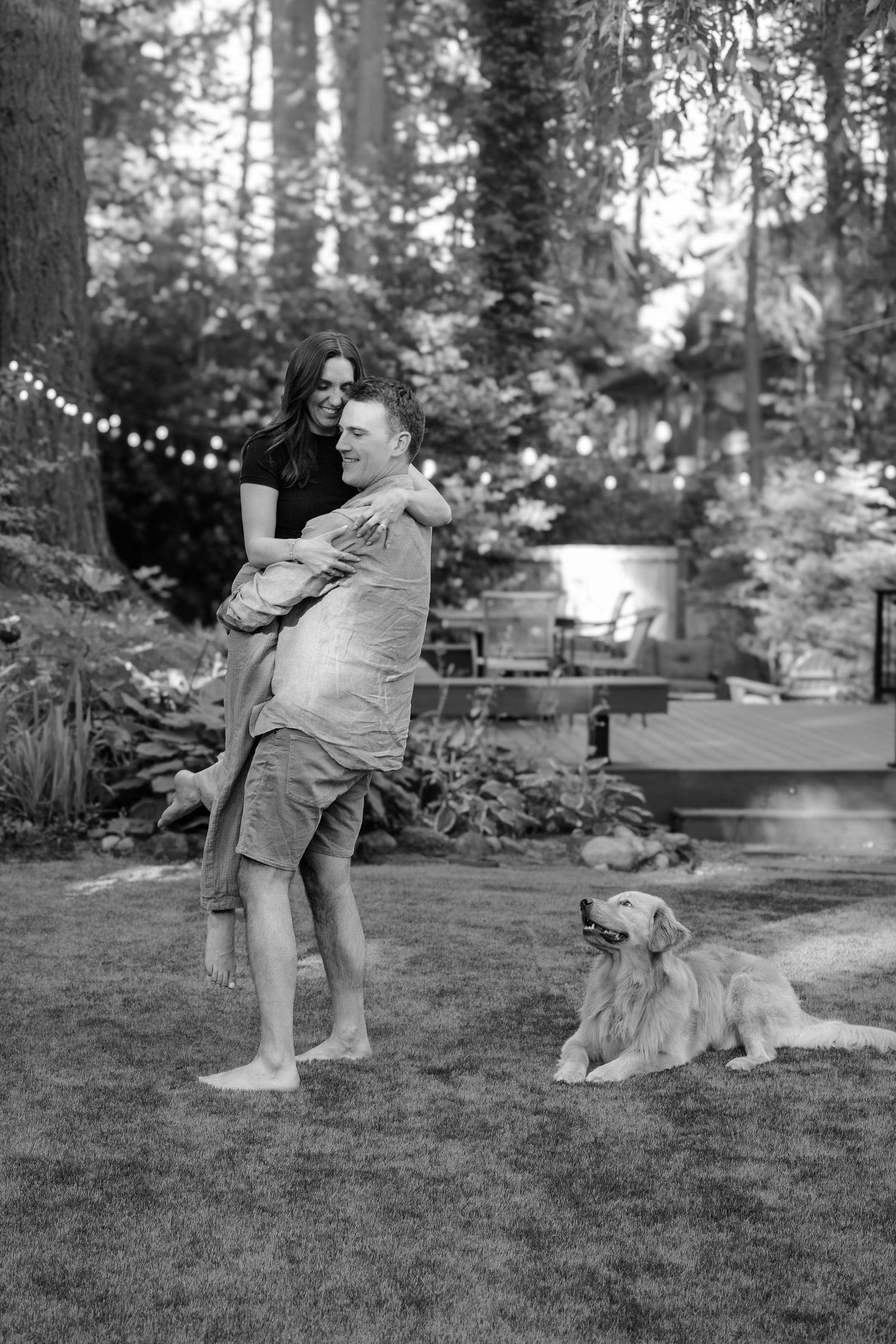 A black and white backyard portrait with string lights and a golden retriever lounging on the grass.