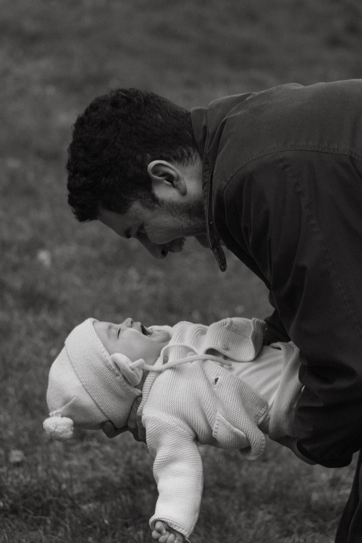 A black and white photograph showing a tender moment of an adult bending down towards a baby lying on the grass.
