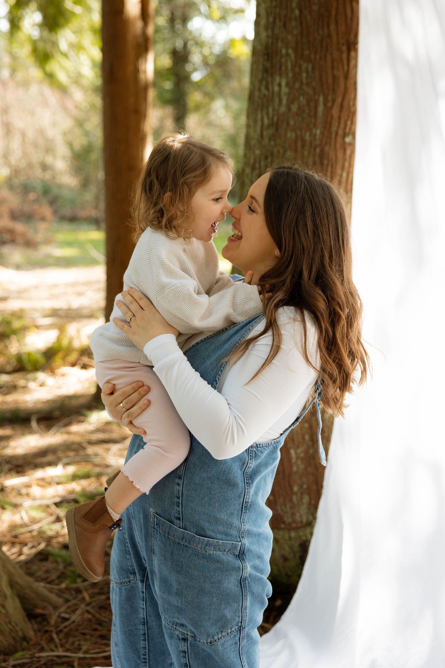 Parent and toddler sharing intimate moment against white backdrop in wooded setting.