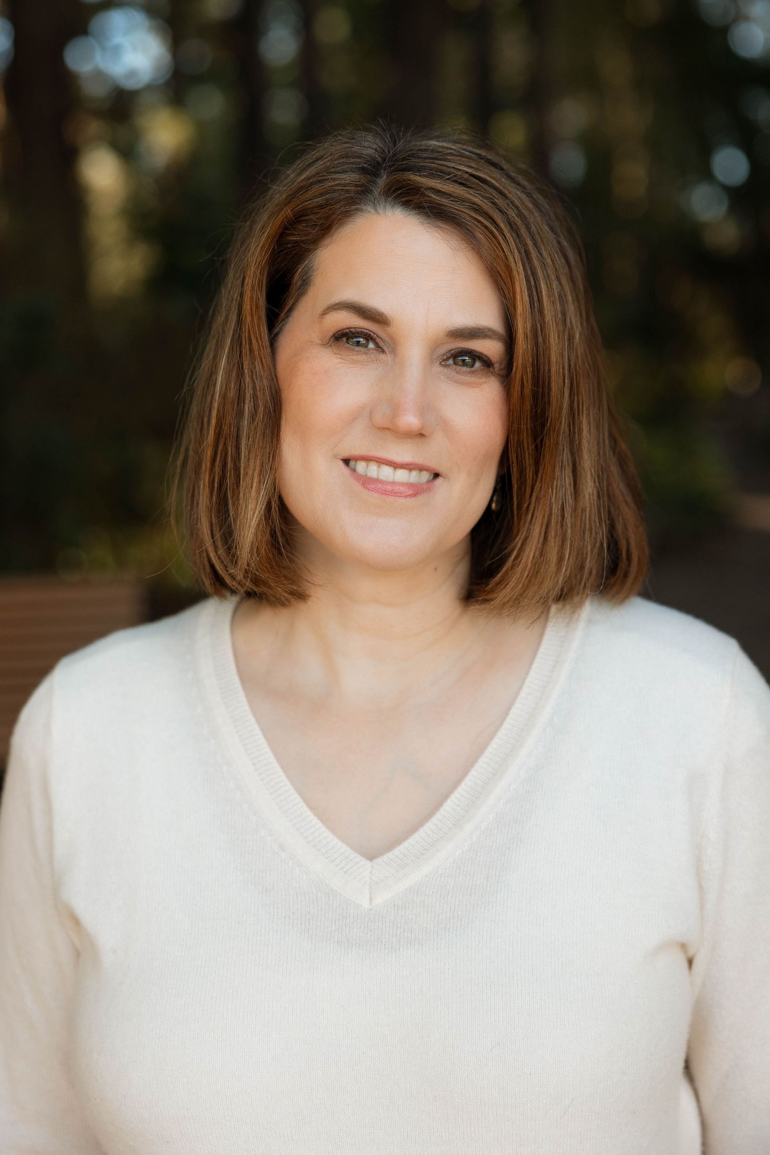 Portrait of person in cream v-neck sweater against blurred outdoor background.