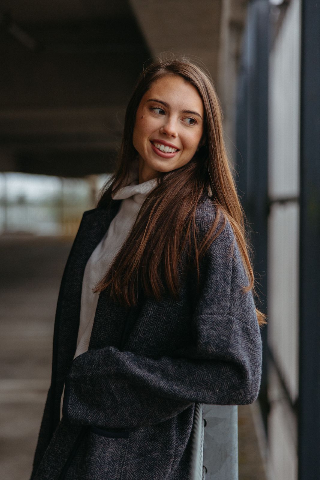 Indoor portrait wearing dark winter coat and white scarf in urban setting.