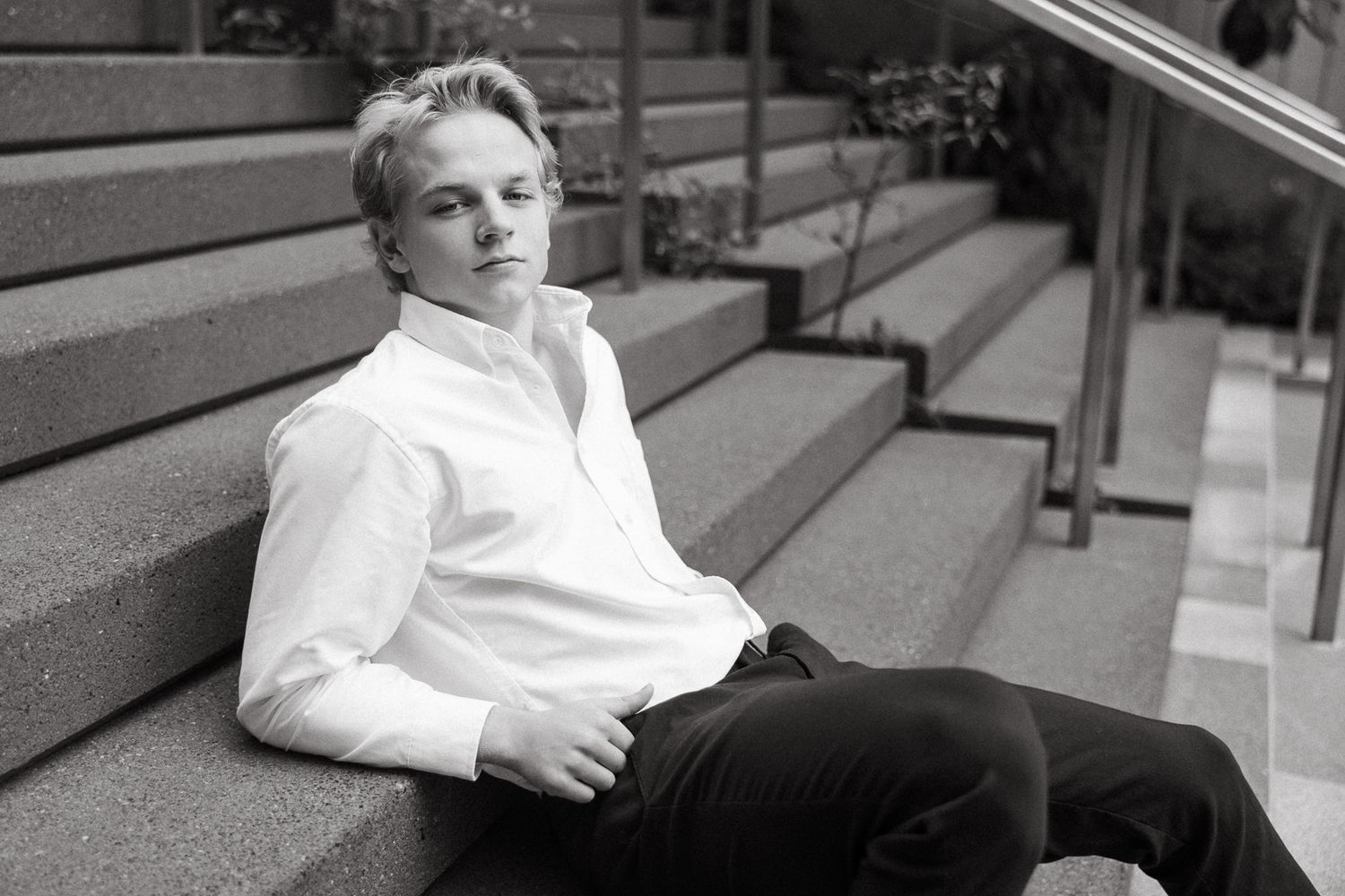 Black and white portrait of a person relaxing on concrete steps in casual attire.