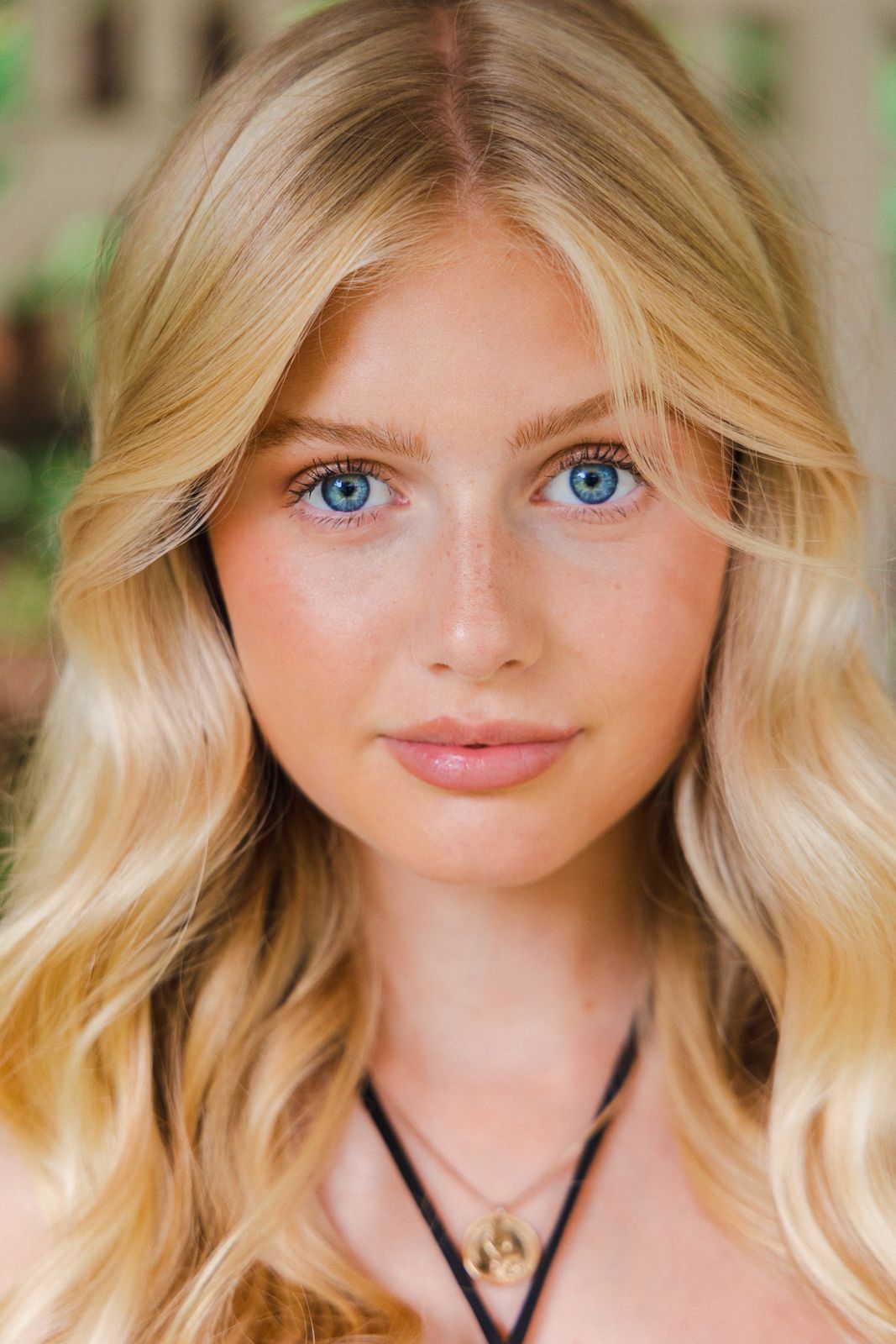 Portrait of person with wavy blonde hair and blue eyes wearing black necklace.