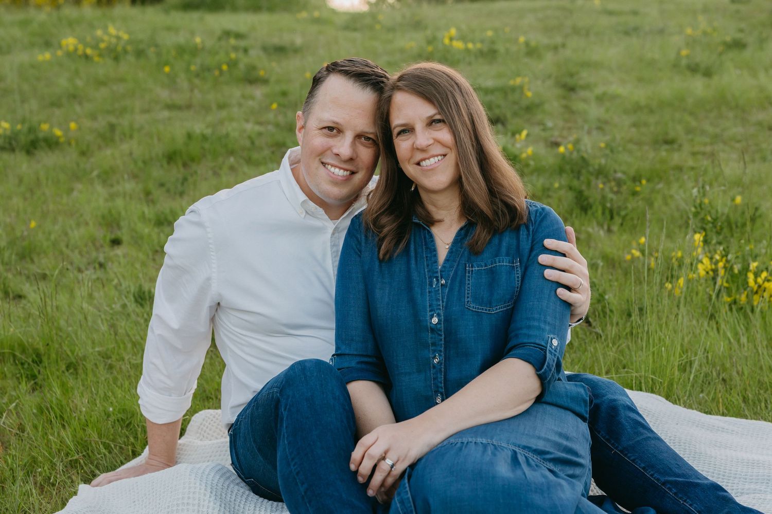 Couple sitting together and smiling on a grassy lawn path during a romantic outdoor photo session.
