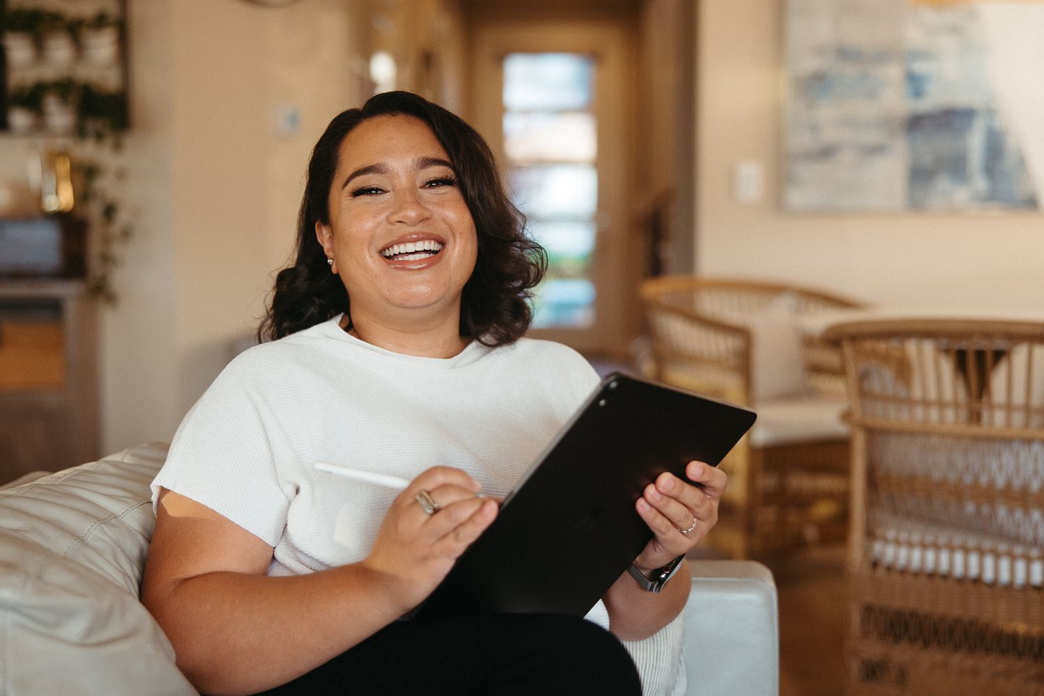 Person smiling while using a tablet device in a cozy home setting.