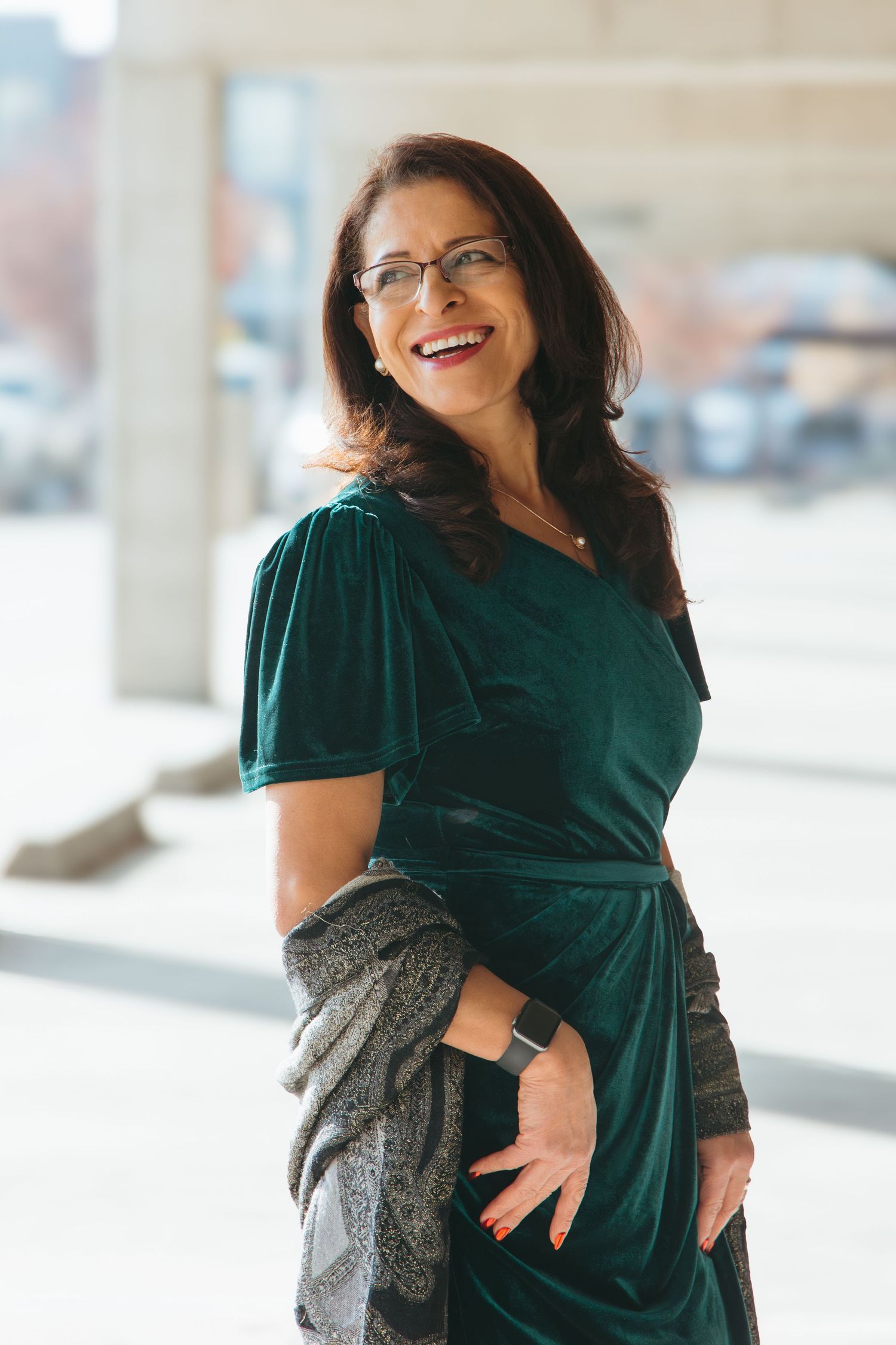 Person wearing emerald green velvet dress and glasses in bright indoor setting.