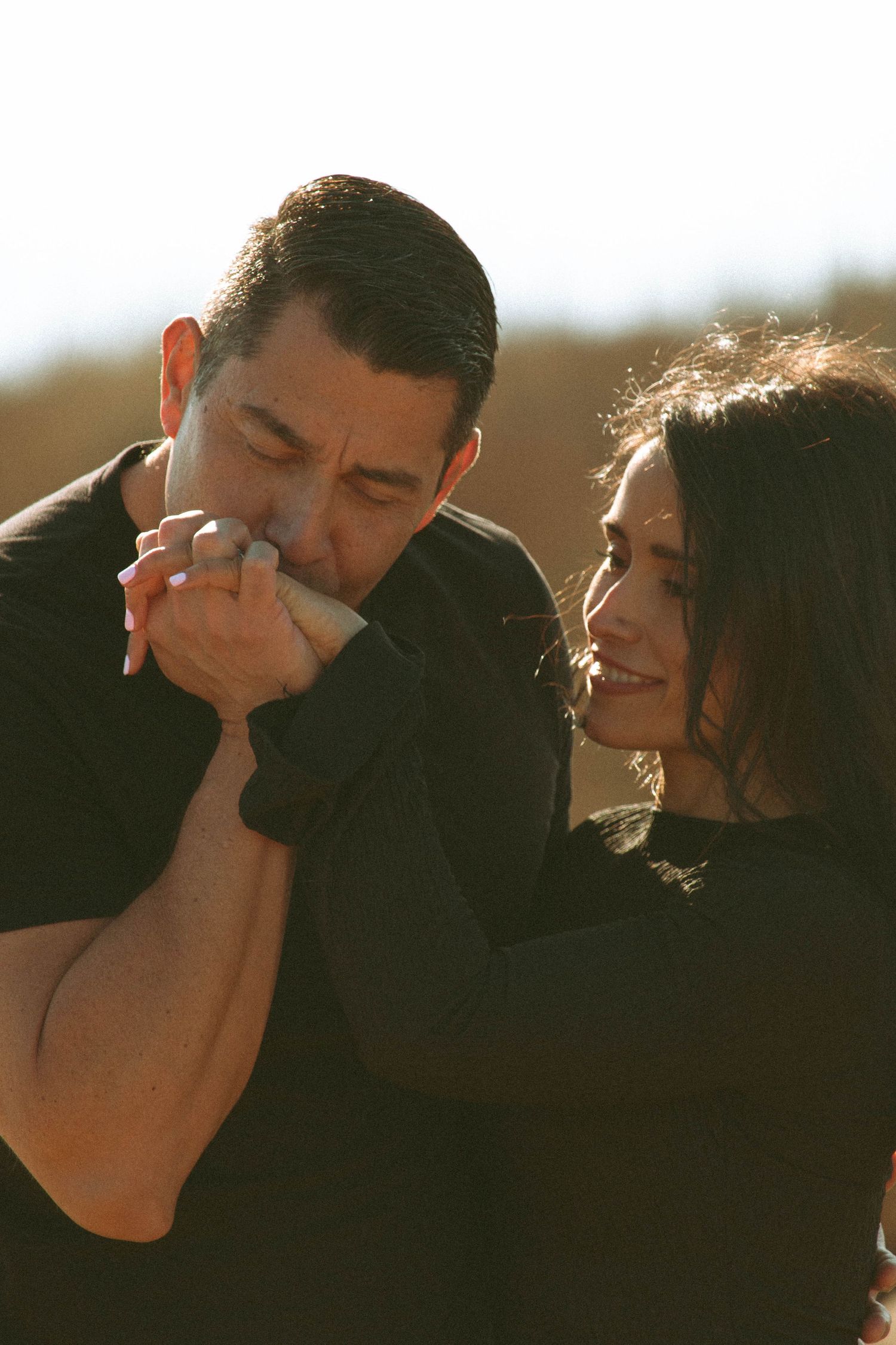 Tender moment between couple as person kisses partner's hand in golden sunlight.