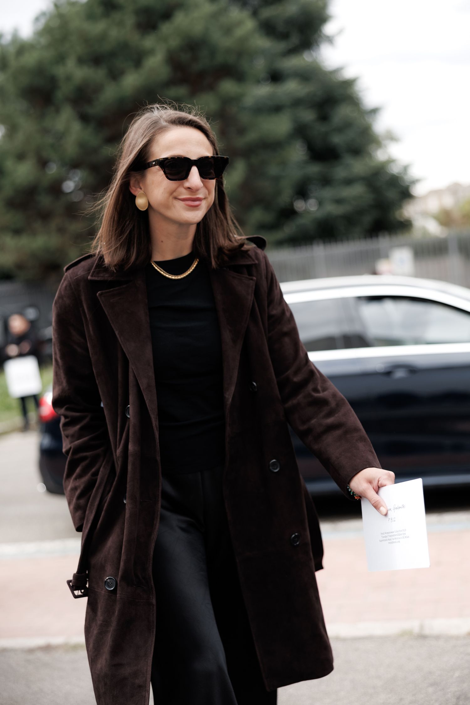 Person wearing a brown fur coat and black outfit walks confidently in an outdoor setting.