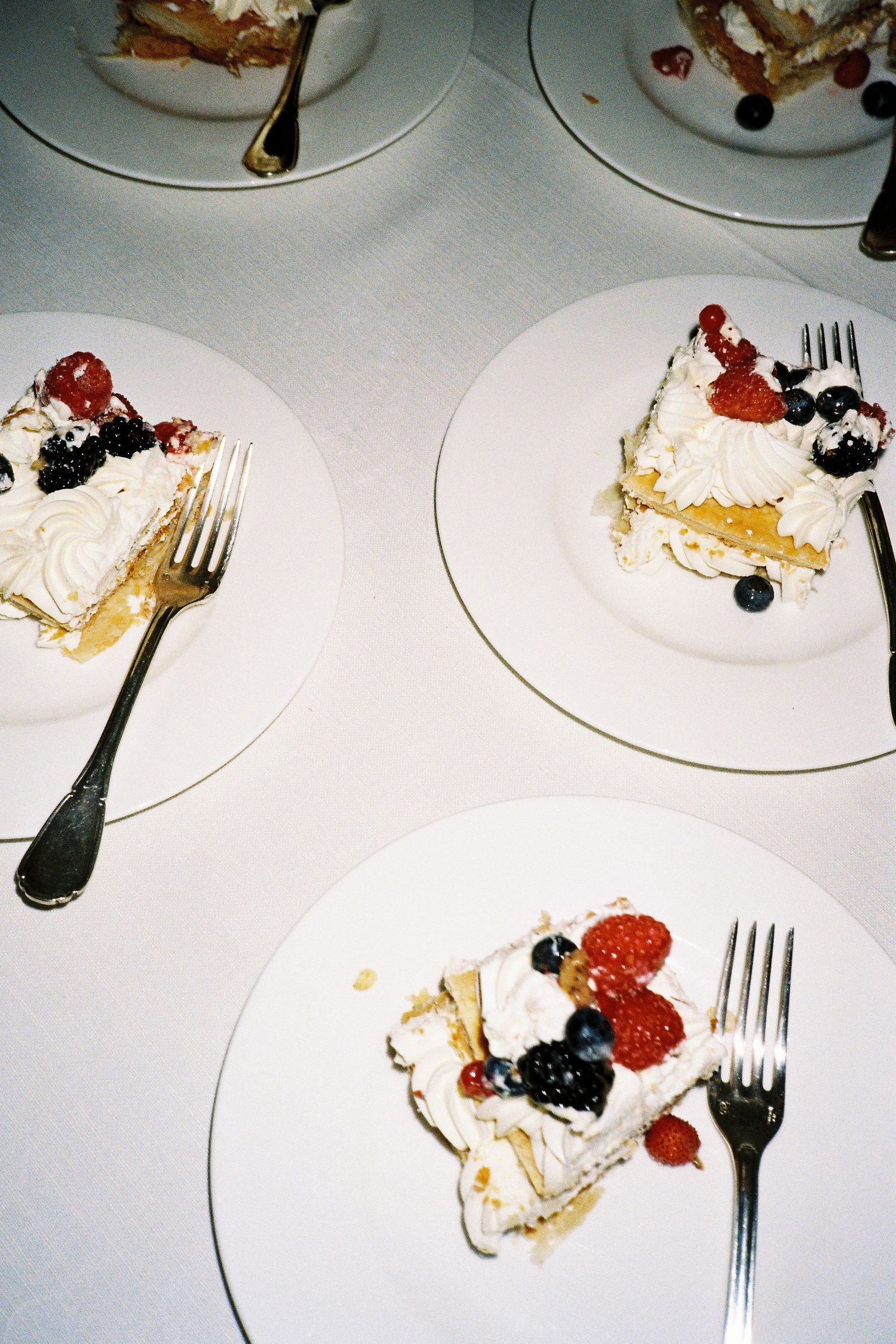 Half-eaten dessert plates with whipped cream, berries and crumbs scattered across multiple white dishes with forks.