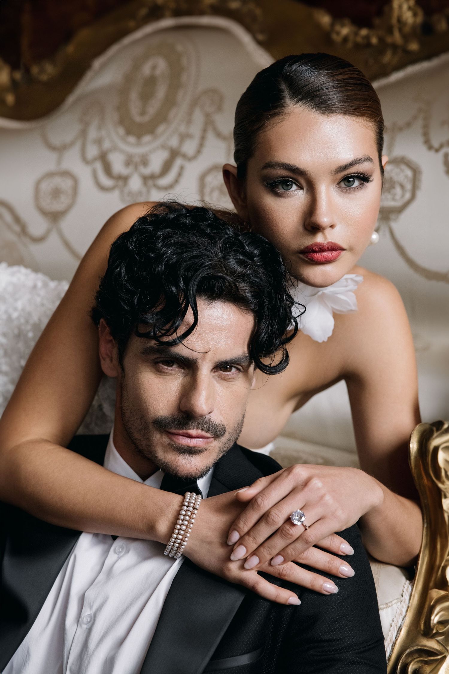 Glamorous formal portrait of couple in evening wear on ornate vintage sofa.