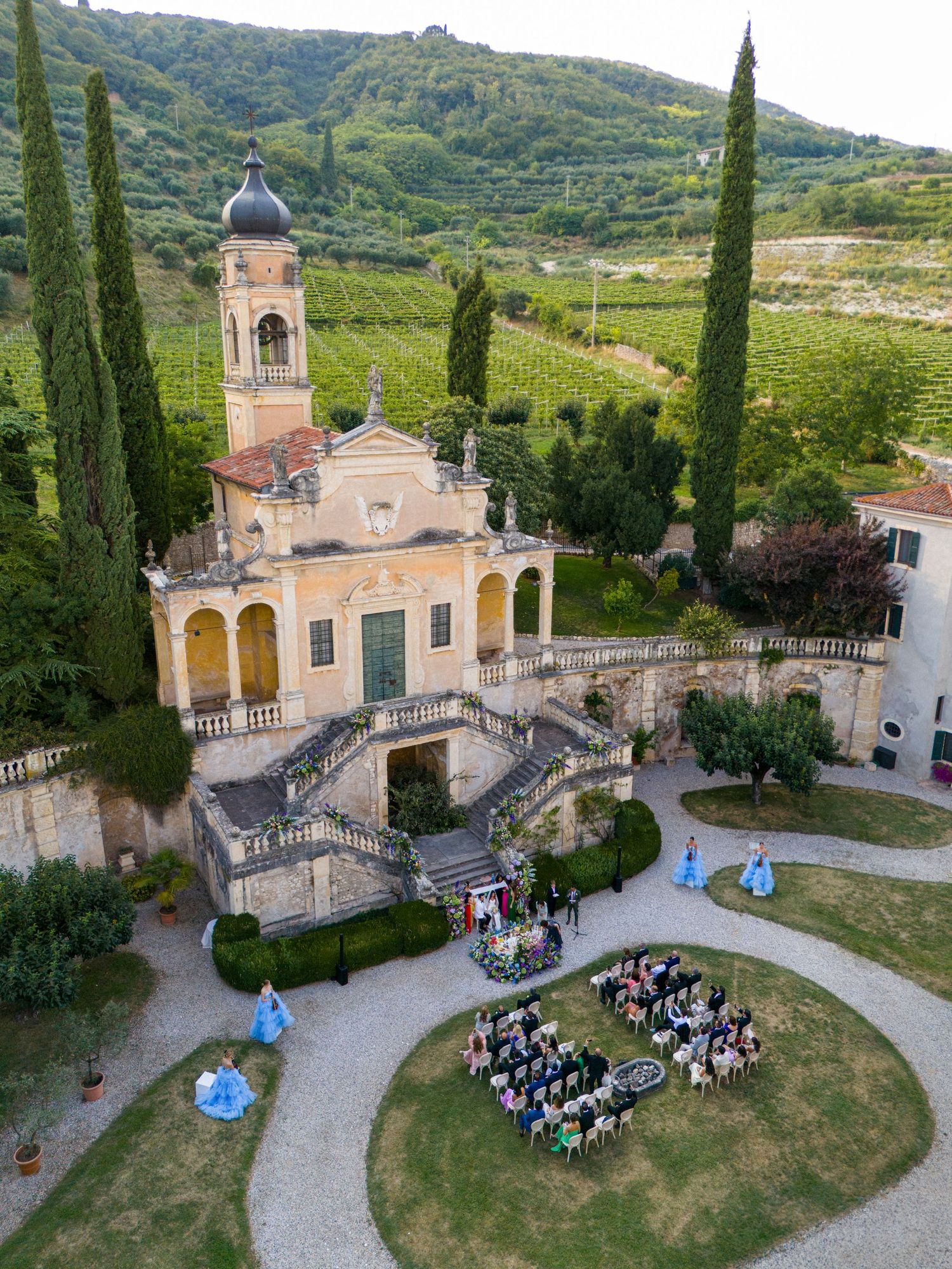 Italian chapel with cypress trees hosts an intimate outdoor wedding ceremony in a vineyard setting.