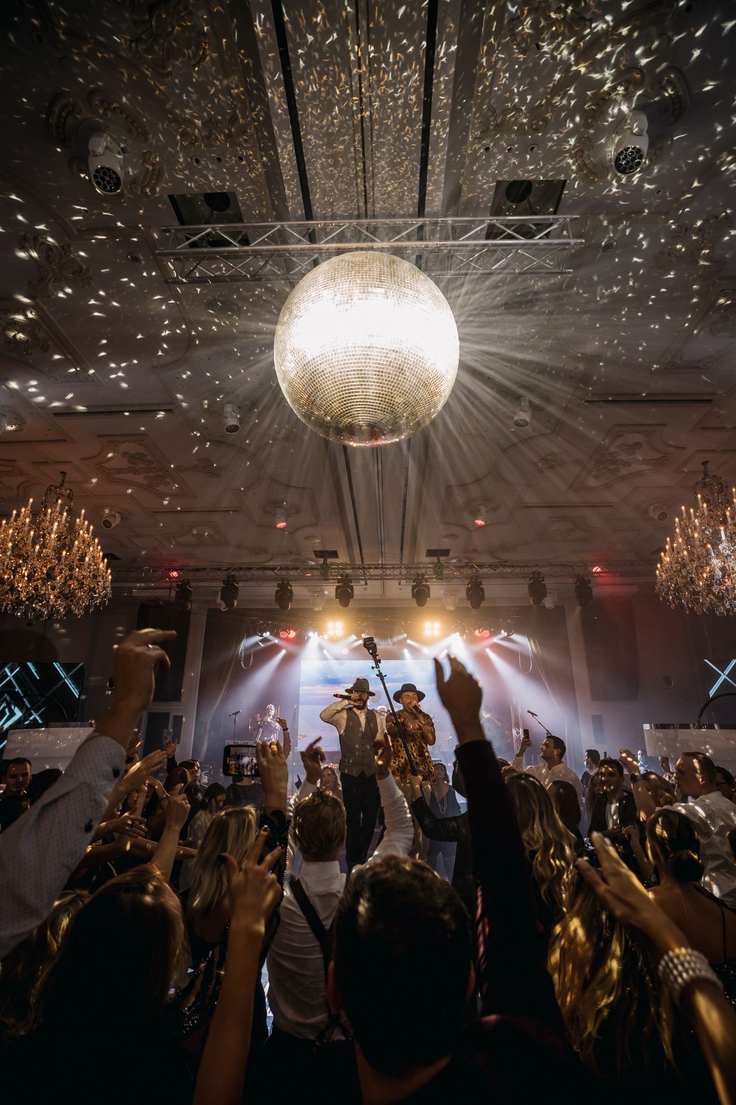 A disco ball illuminates a crowded concert venue with sparkles and light beams.