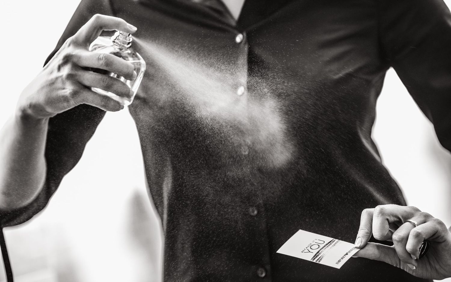 Black and white close-up of hands spraying perfume creating a fine mist.