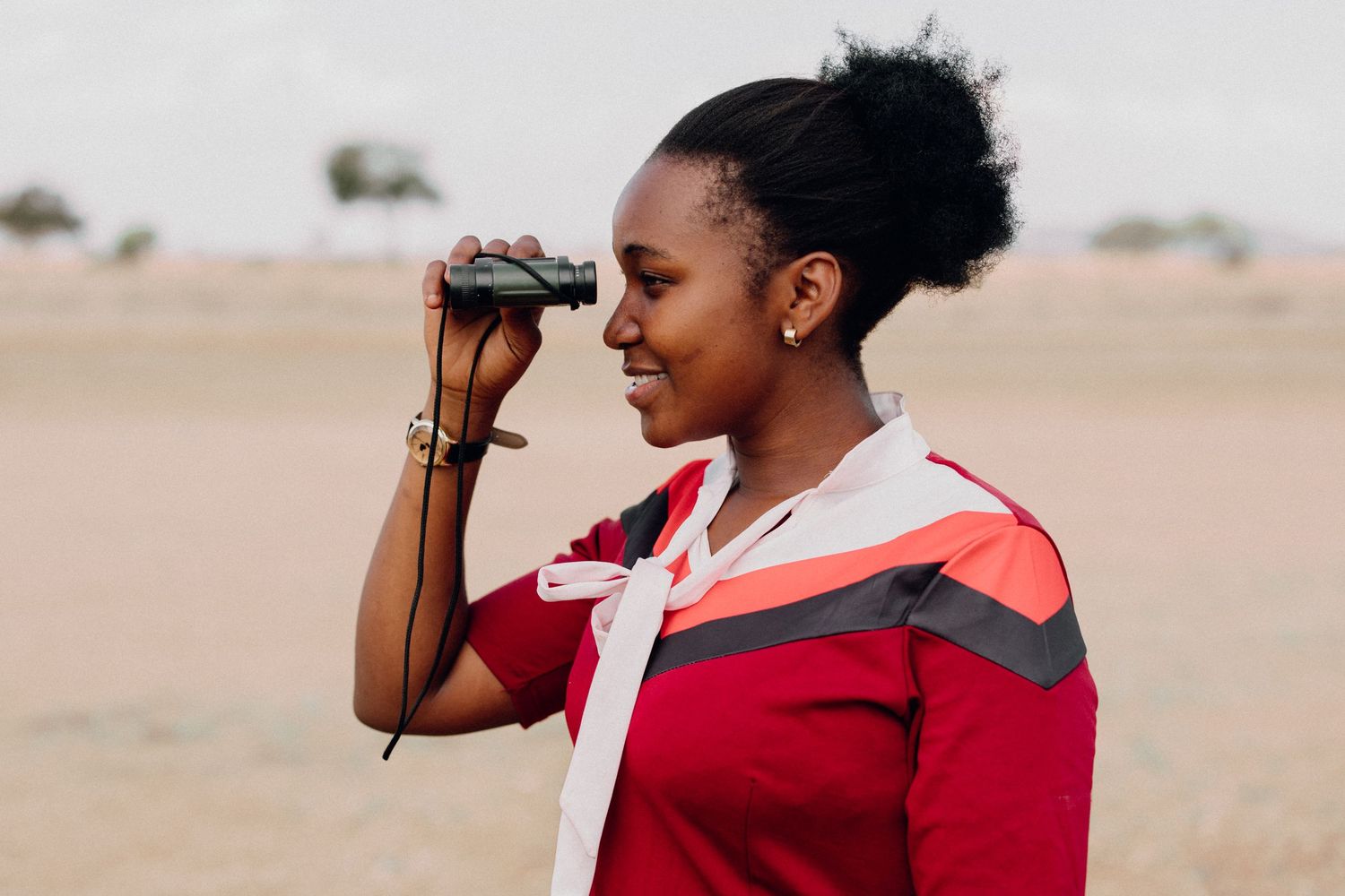 Person in red sportswear using binoculars while exploring outdoors.