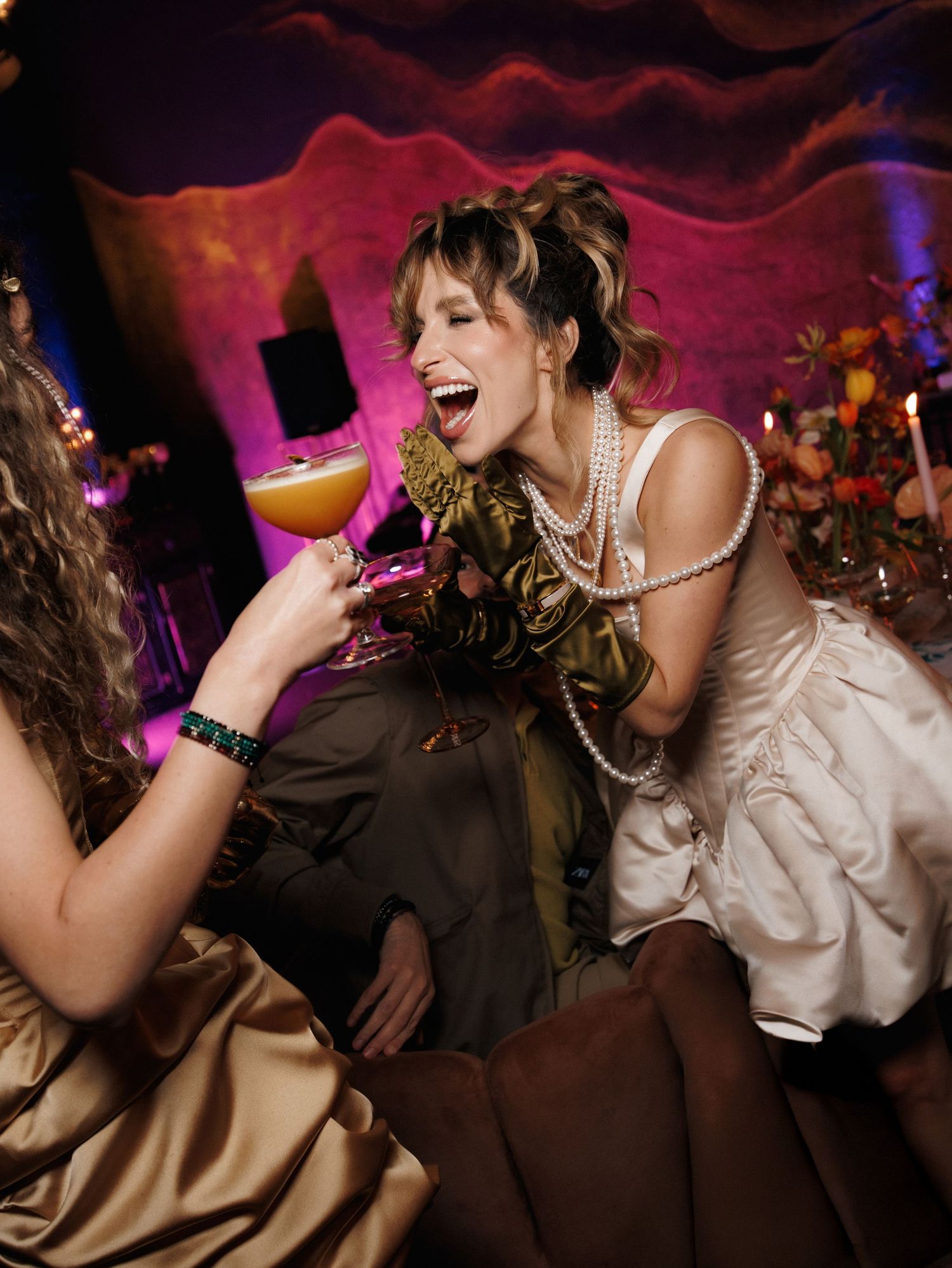 Wedding guests dancing and laughing together on a vibrant pink-lit dance floor during reception celebrations.