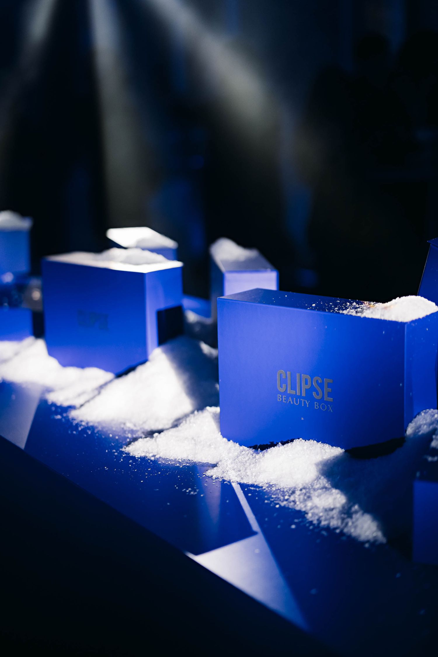 Blue gift boxes arranged on a surface with snow-like powder in dramatic lighting.