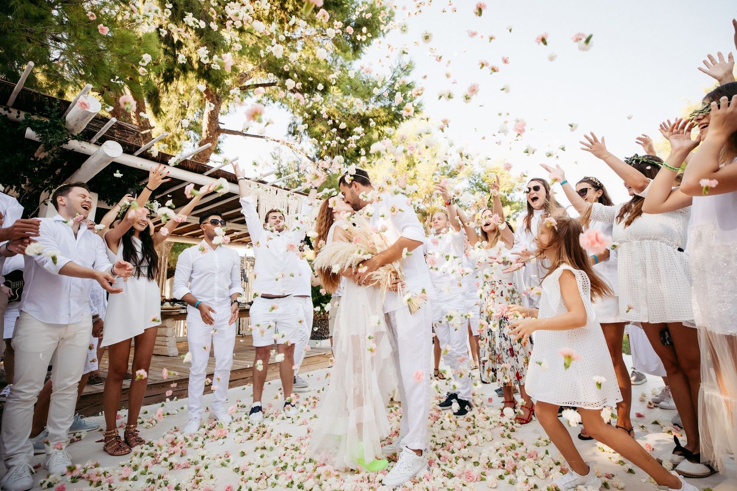 Wedding celebration with guests throwing confetti at a white-themed outdoor ceremony.