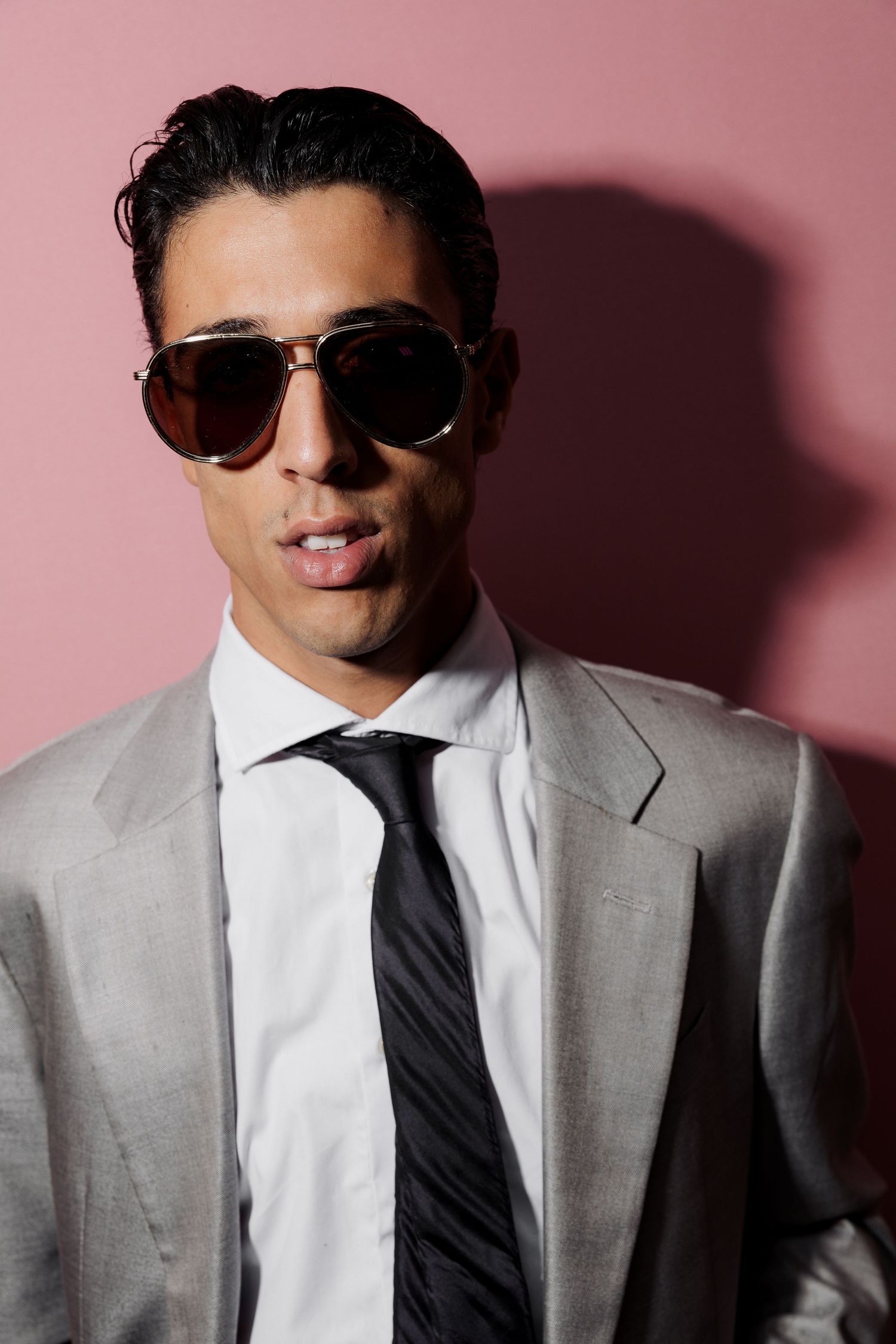 Fashion portrait series showing a model in a light gray suit and sunglasses against a pink background.