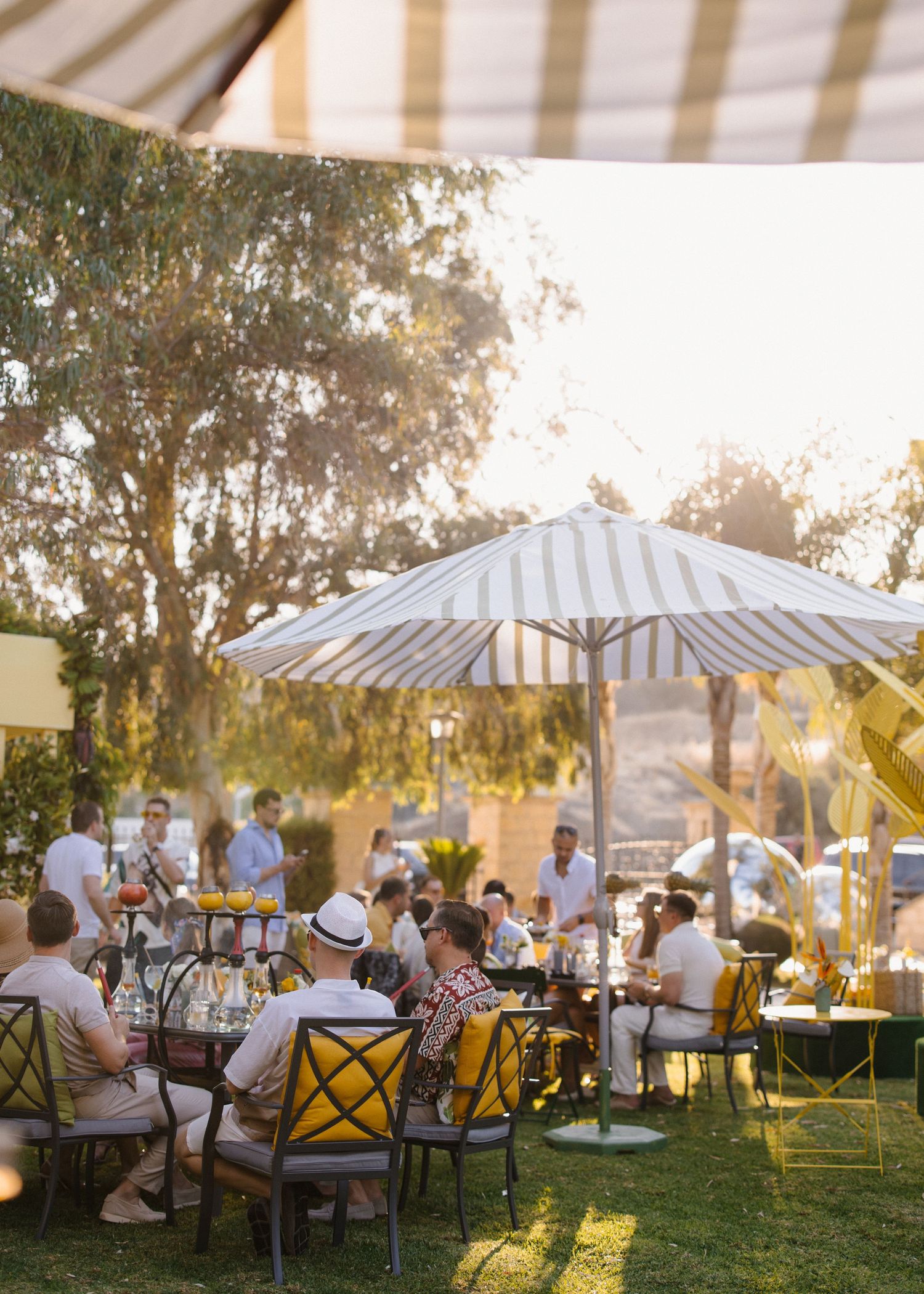 Outdoor garden party setting with striped umbrellas and casual seating at sunset.