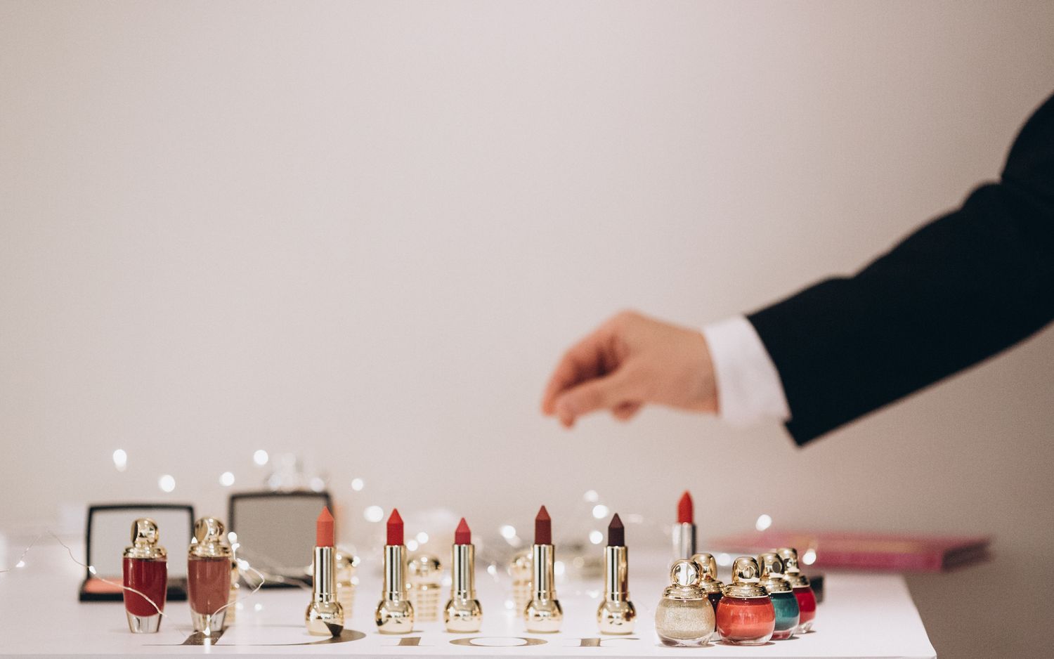 Collection of luxury lipsticks arranged on white surface with hand reaching to select one.