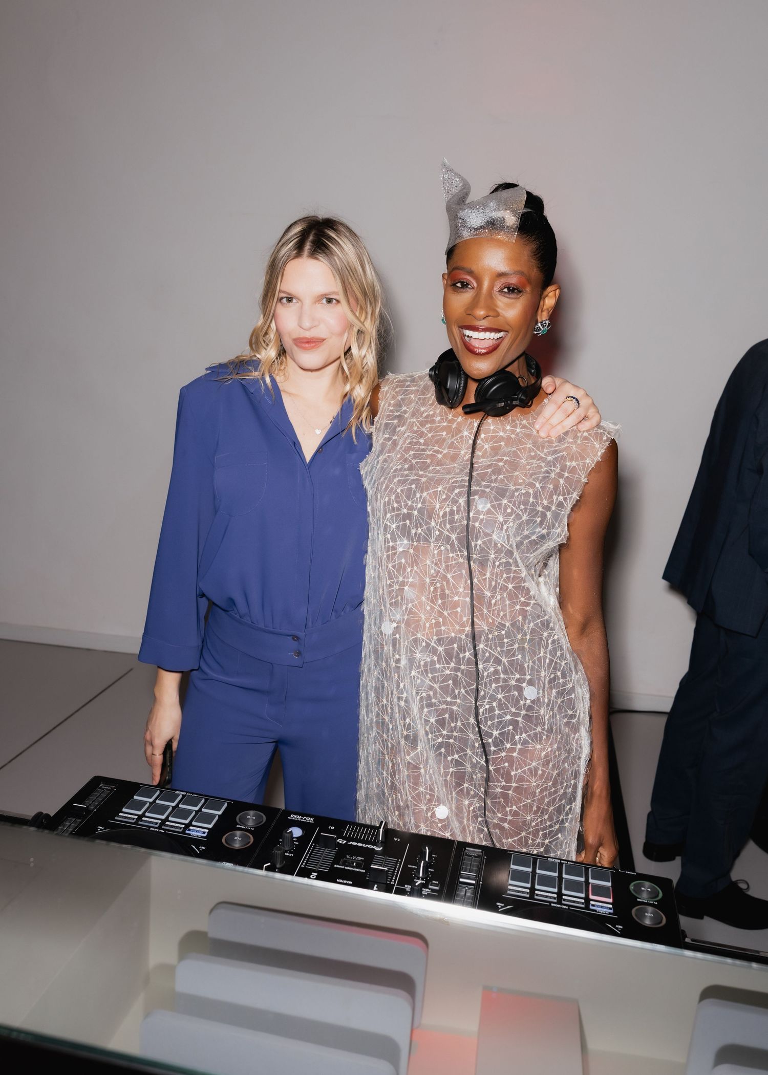 Two people pose together at a DJ booth wearing contrasting blue and sparkly outfits.